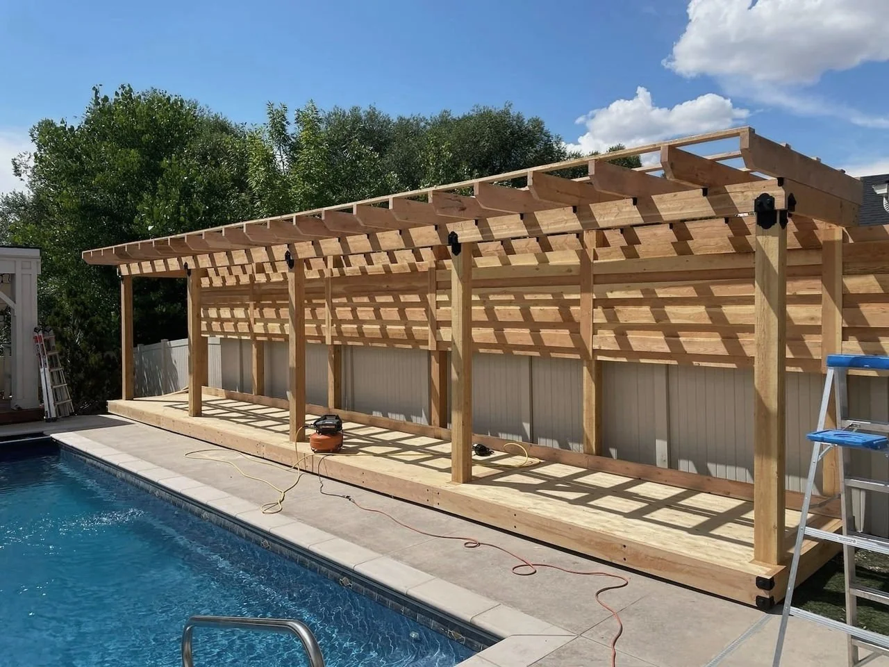 Backyard pergola near a blue water pool. Sunset Decks.