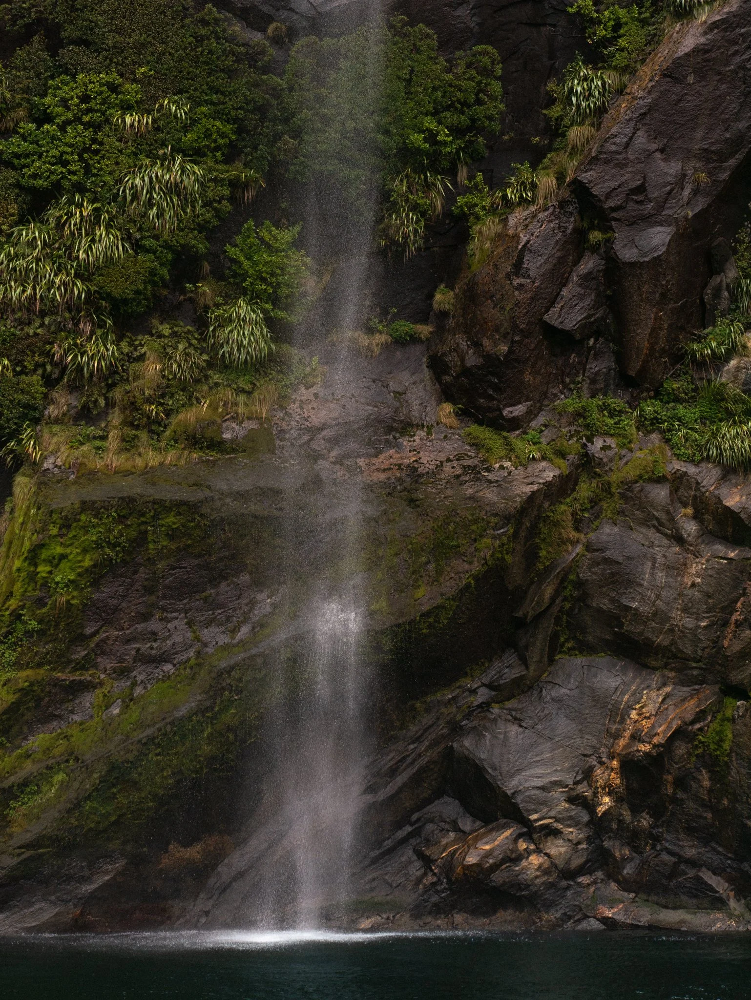 Milford sound waterfall cascading over rocks with lush green vegetation.