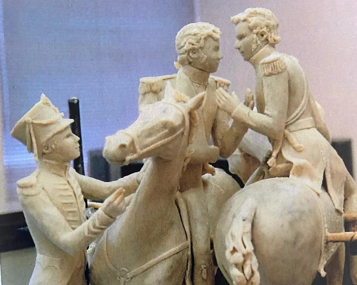 A beige sculptural group of soldiers in military uniforms engaged in a battle scene, with one soldier on a horse and others interacting with each other.