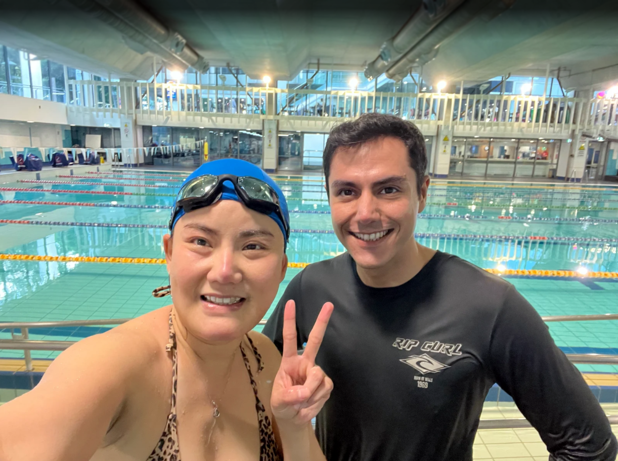 An adult student with a swim teacher standing at the edge of a swimming pool