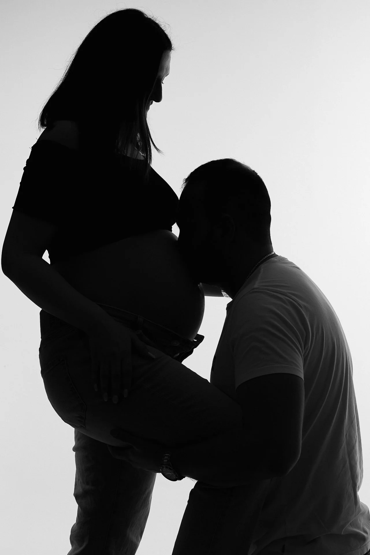 Silhouette eines Paares, bei dem der Mann den Kopf an den Bauch der schwangeren Frau legt, die ihn liebevoll hält.