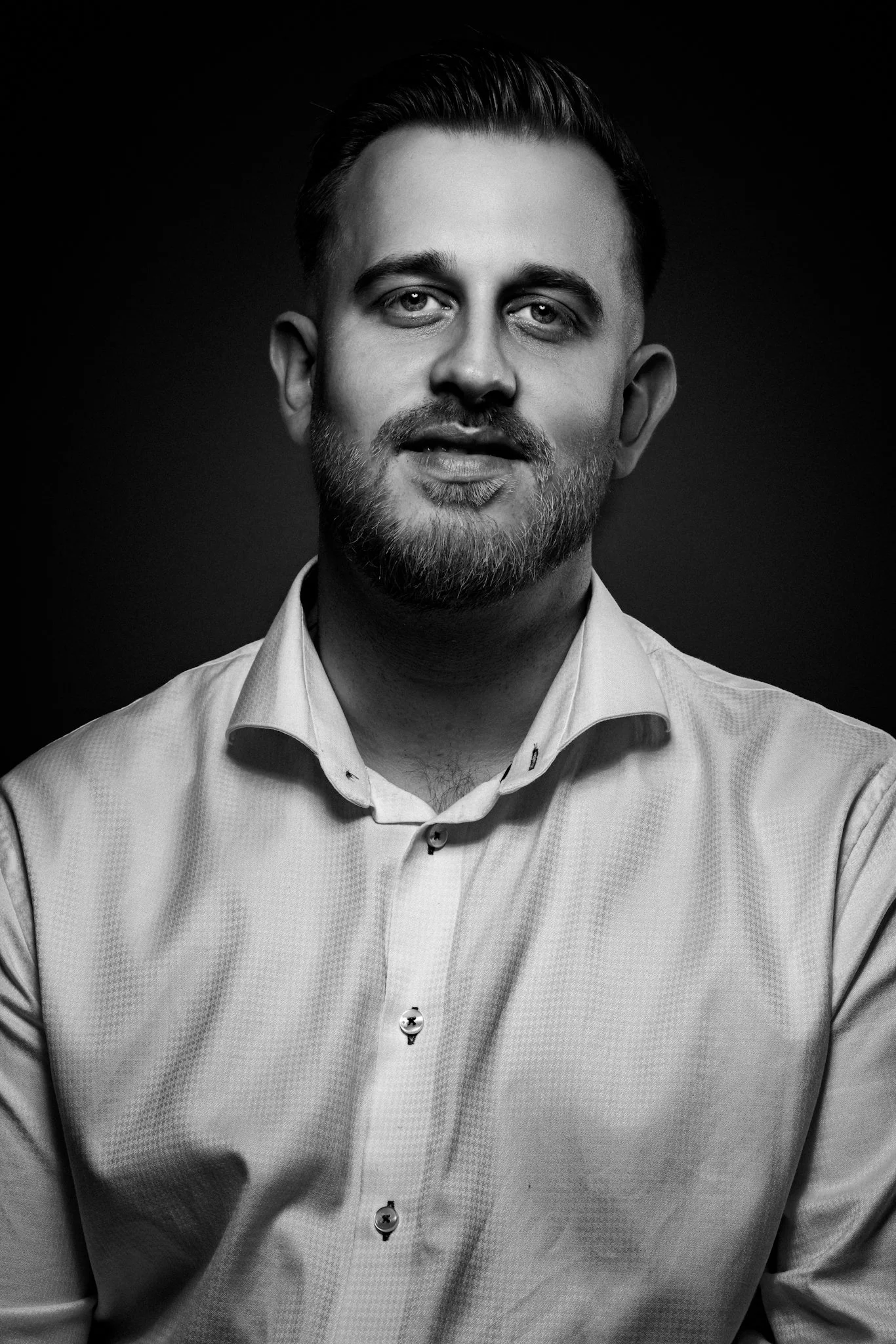 Schwarz-Weiß-Porträt eines Mannes mit kurz, dunklem Haar, Bart und gepflegtem Aussehen, trägt ein Hemd.