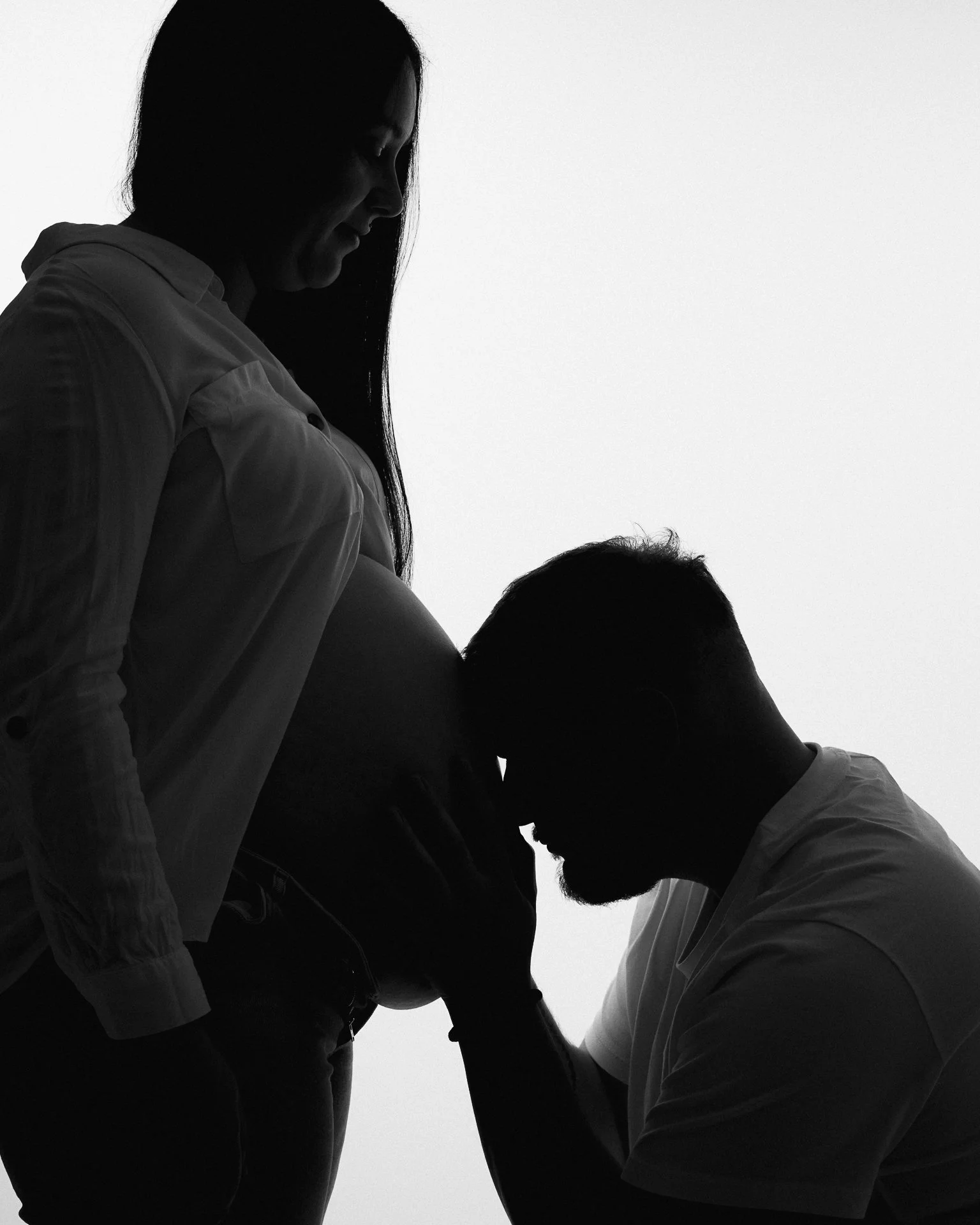 Silhouette eines Paares, das ein Baby im Bauch liebevoll berührt in Schwarz-Weiß