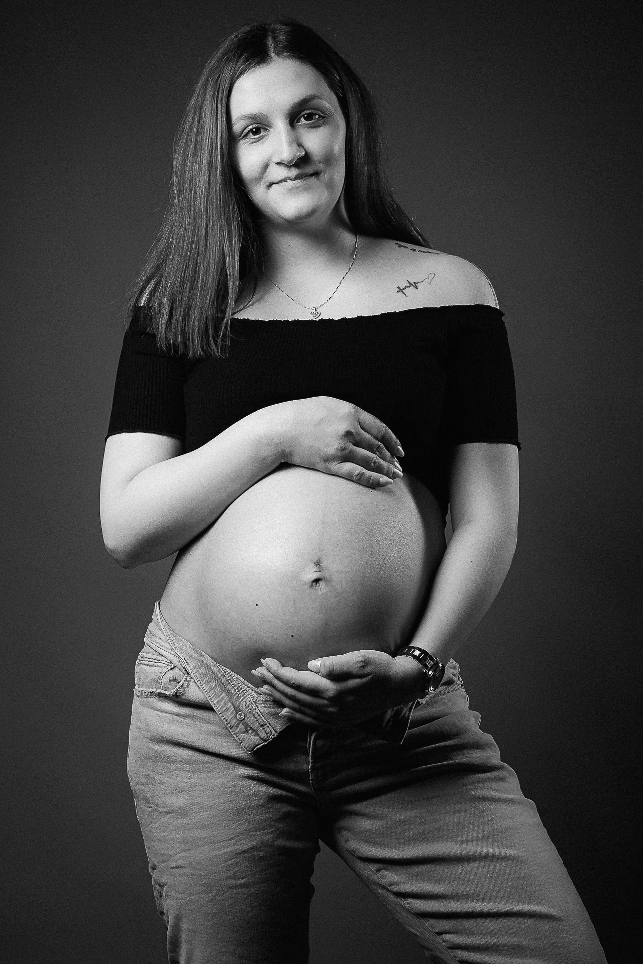 Schwangere Frau in Schwarz-Weiß-Porträt, die ihren Babybauch hält.
