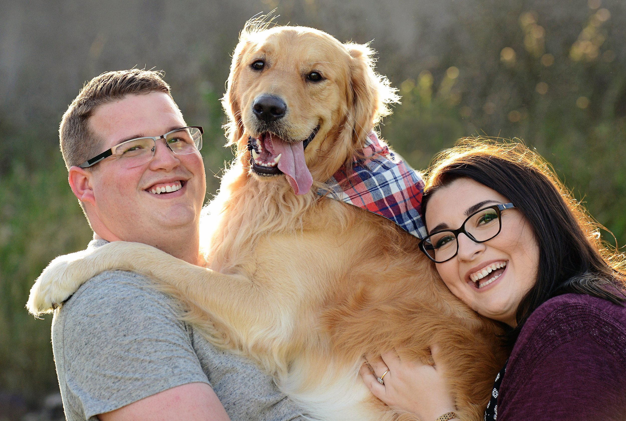 Happy couple holding a golden retriever puppy outdoors during daytime.