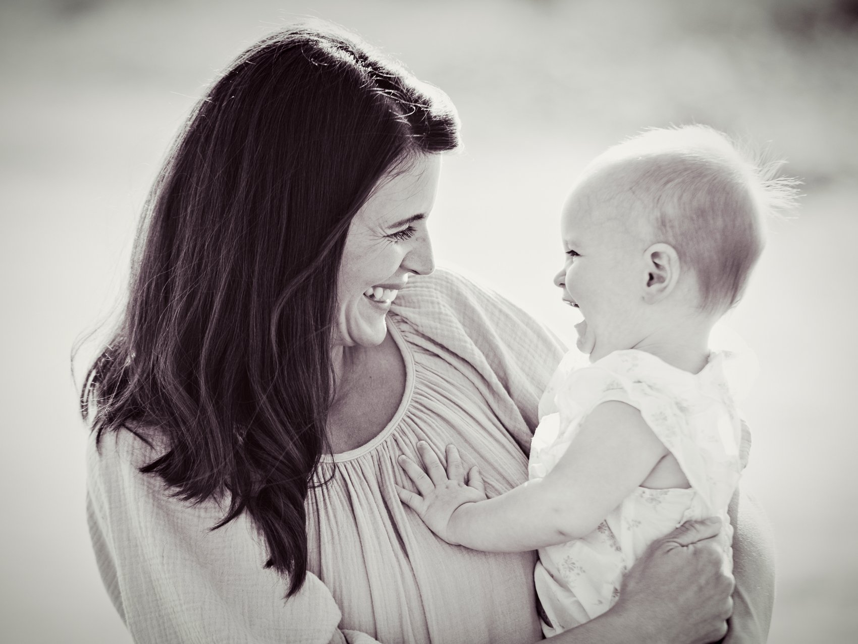 A woman and a baby girl smiling and looking at each other outdoors