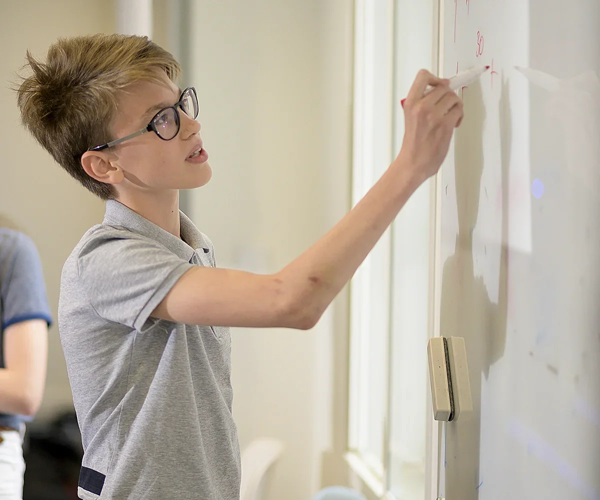 A young boy with glasses writing on a whiteboard with a marker.
