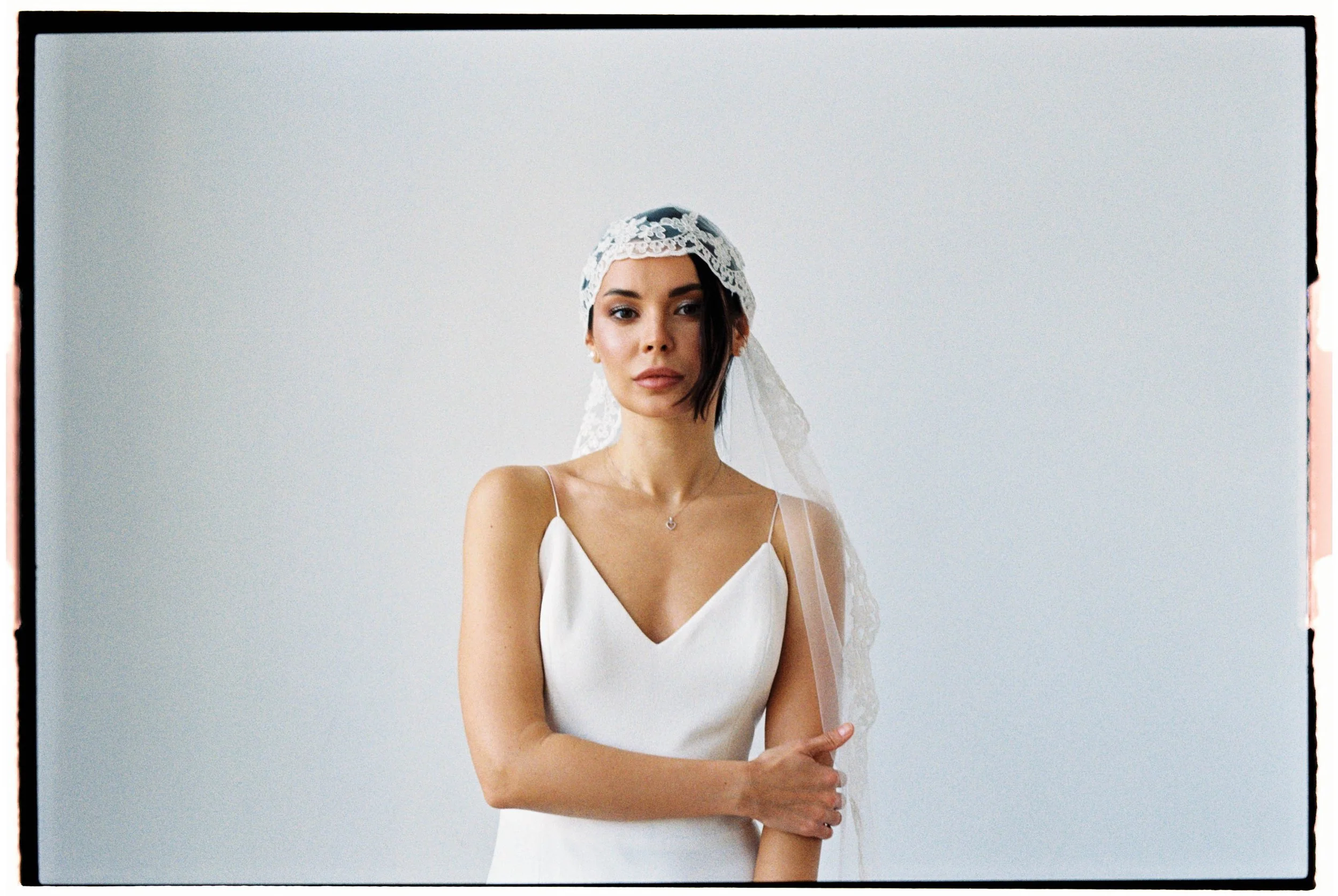 Mujer con vestido de novia y velo, de rostro relajado, posando frente a fondo blanco.
