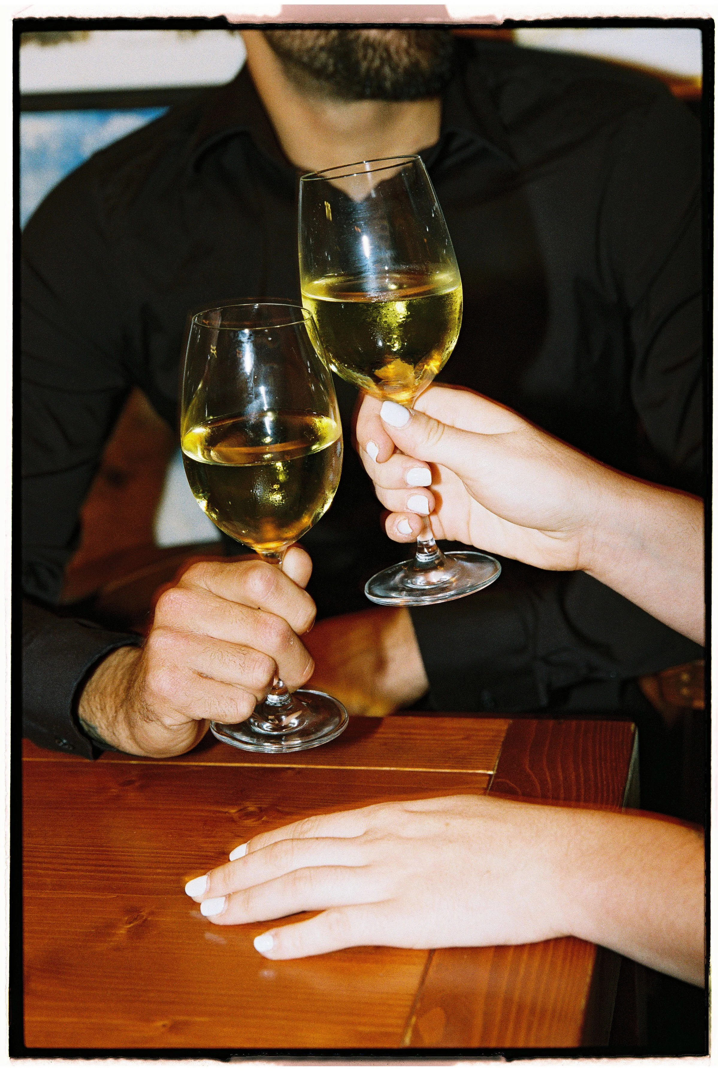 Dos personas brindando con copas de vino blanco en un ambiente de celebración.