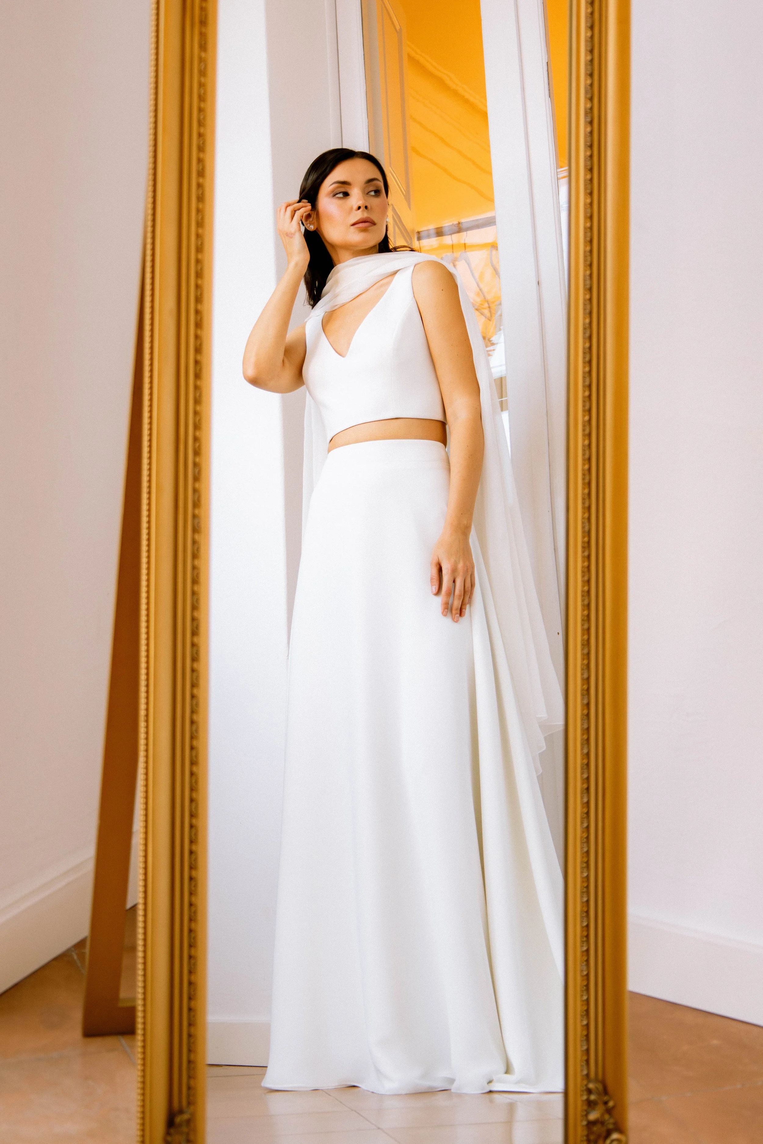 Una mujer vestida con un vestido de novia blanco se mira en un espejo de cuerpo entero.