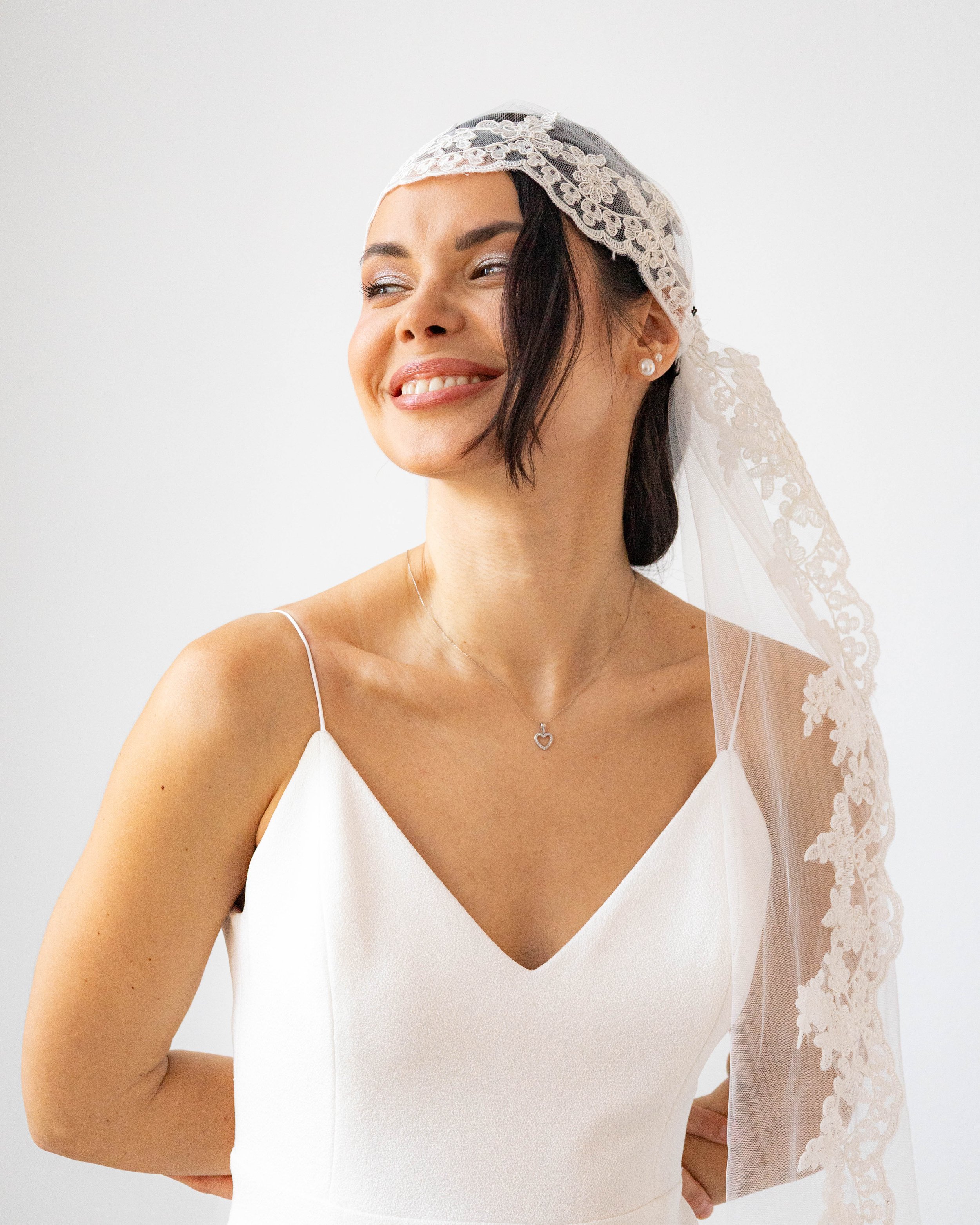 Mujer con vestido de novia, tocado de encaje y velo, sonriendo.