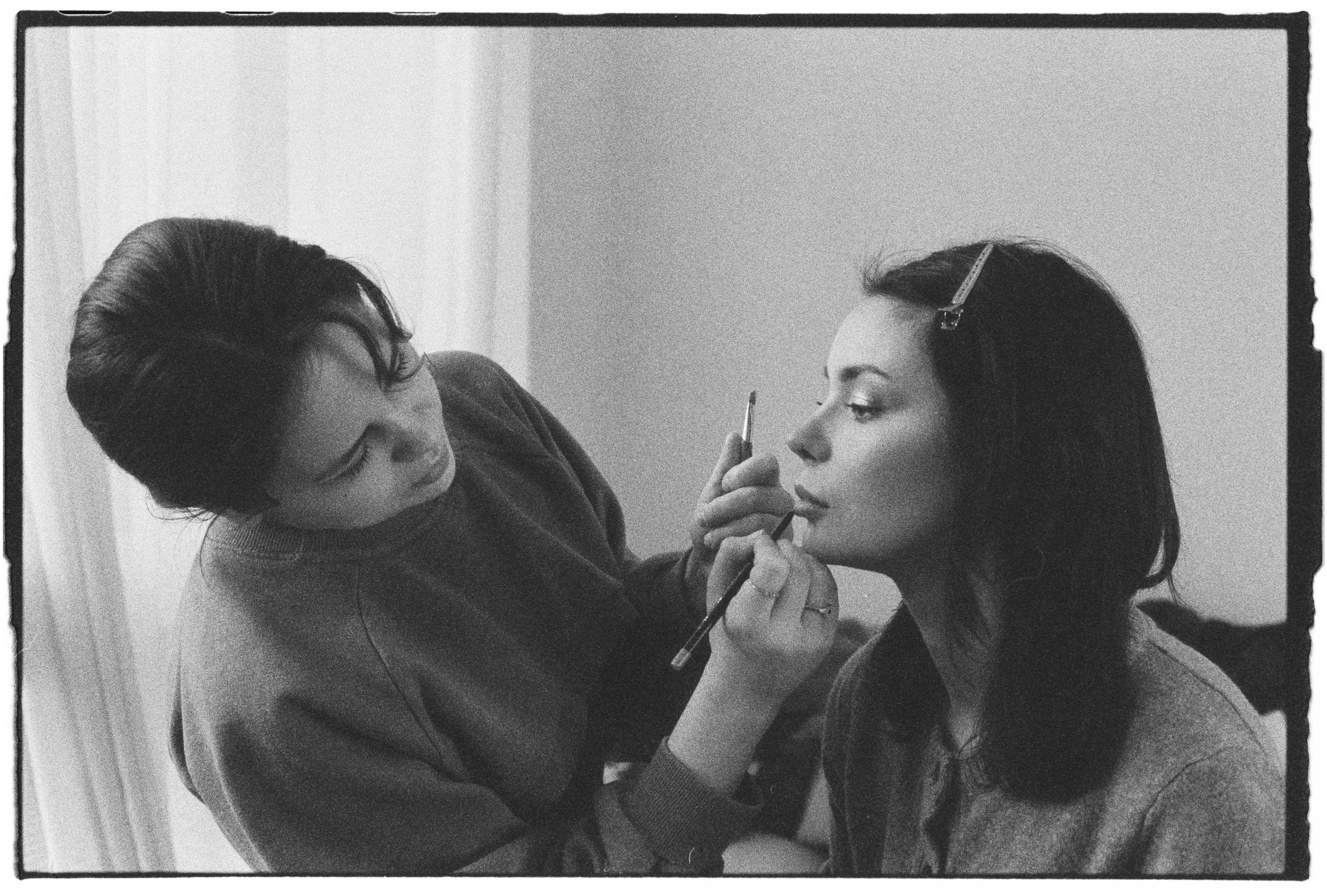 Una mujer maquillándose mientras otra le aplica el maquillaje en su rostro.