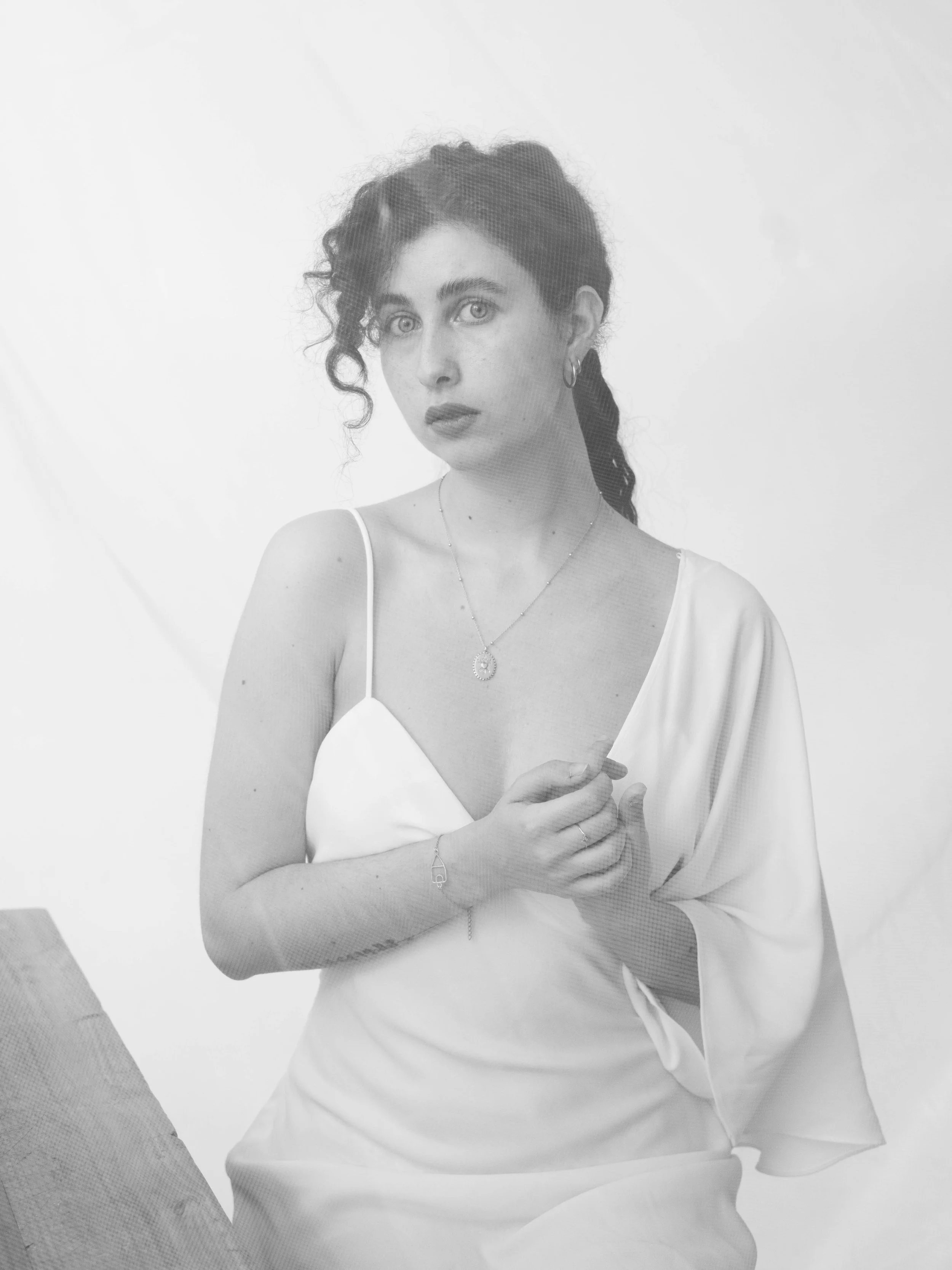 Retrato en blanco y negro de una mujer con cabello rizado y oscuro, sosteniendo sus manos juntas, vestida con un vestido y joyería sencilla.