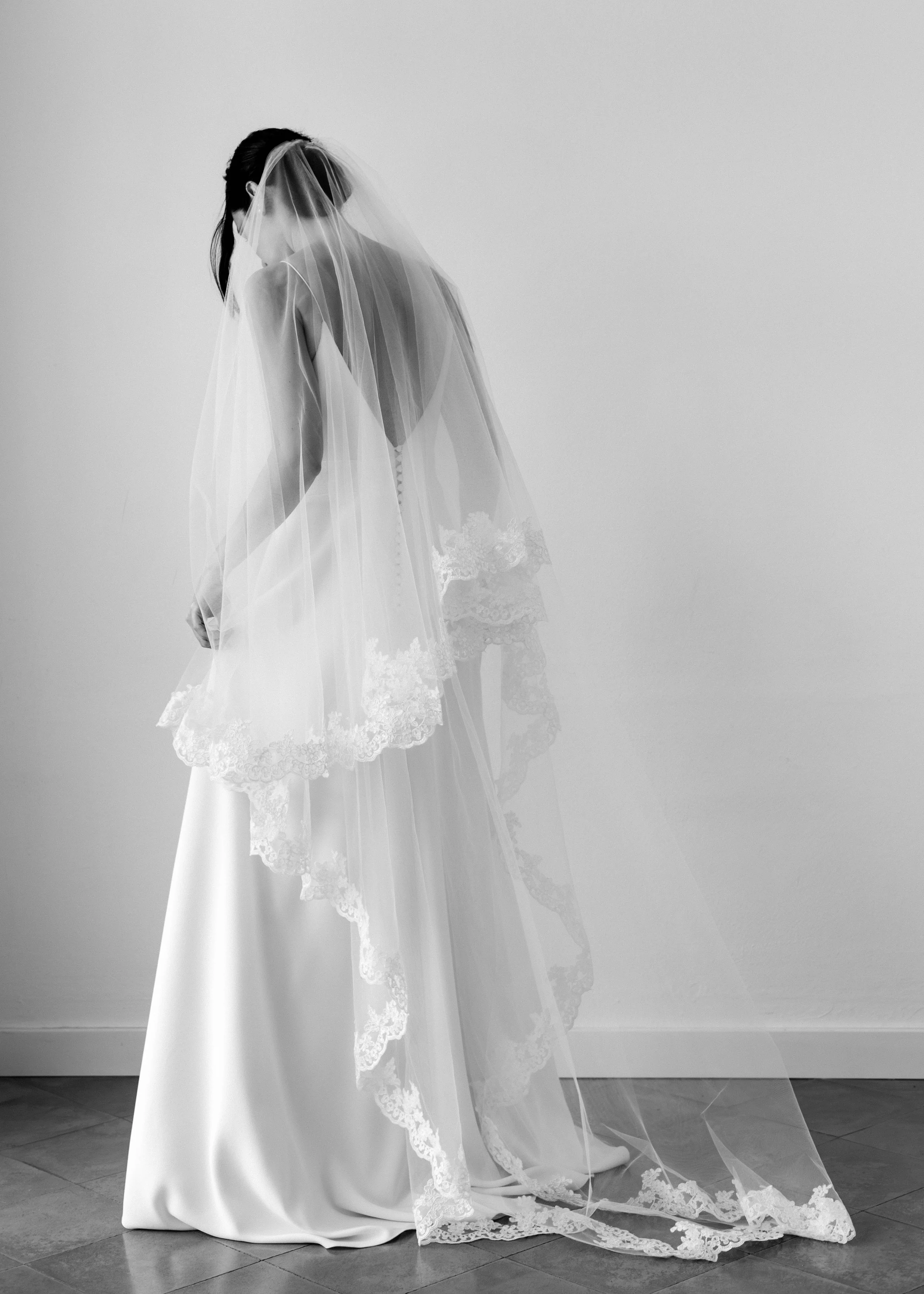 Mujer en vestido de novia con velo, vista de espaldas en blanco y negro.