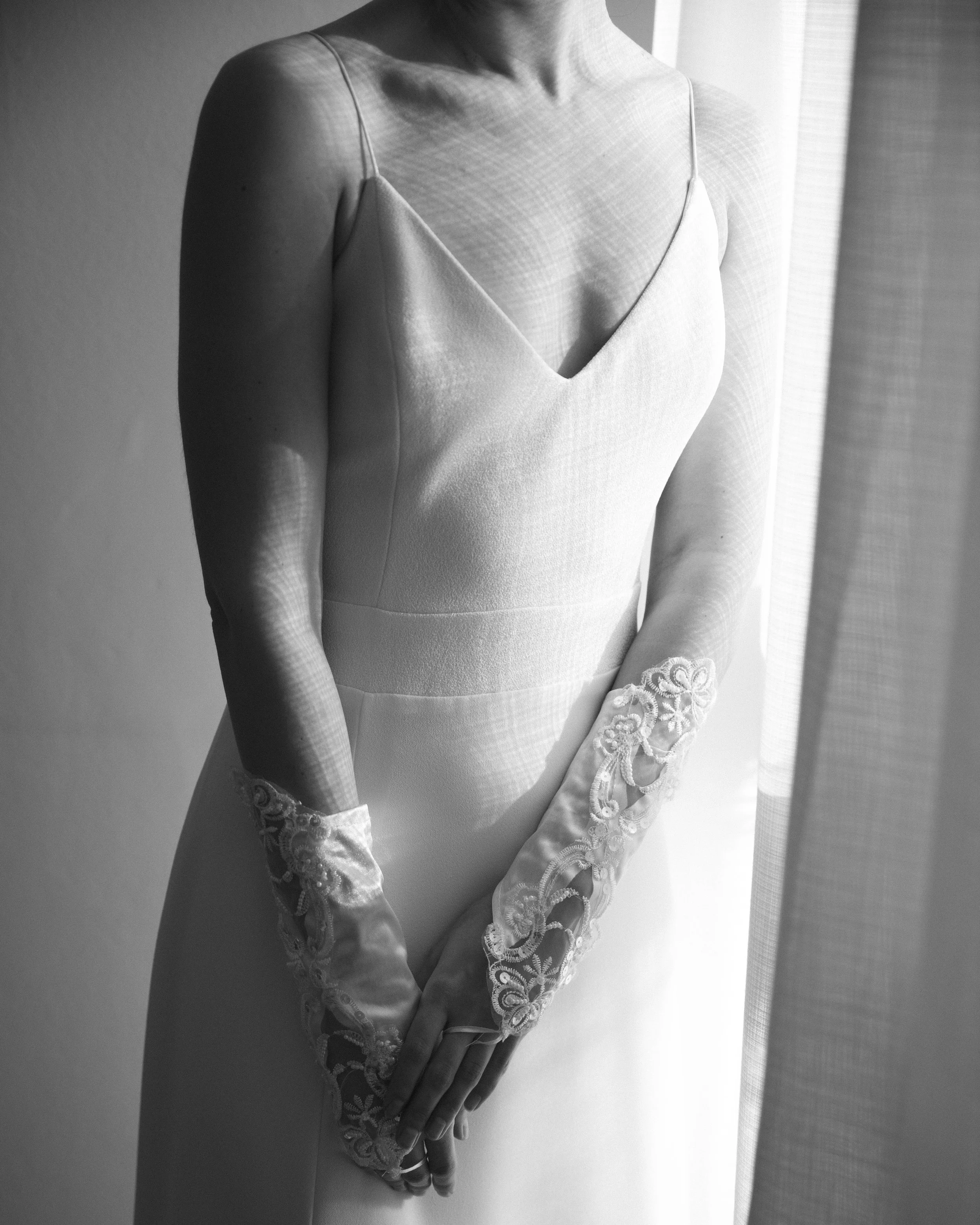 Vestido de novia de encaje y seda, vista parcial en blanco y negro, con manoplas de encaje en las manos.