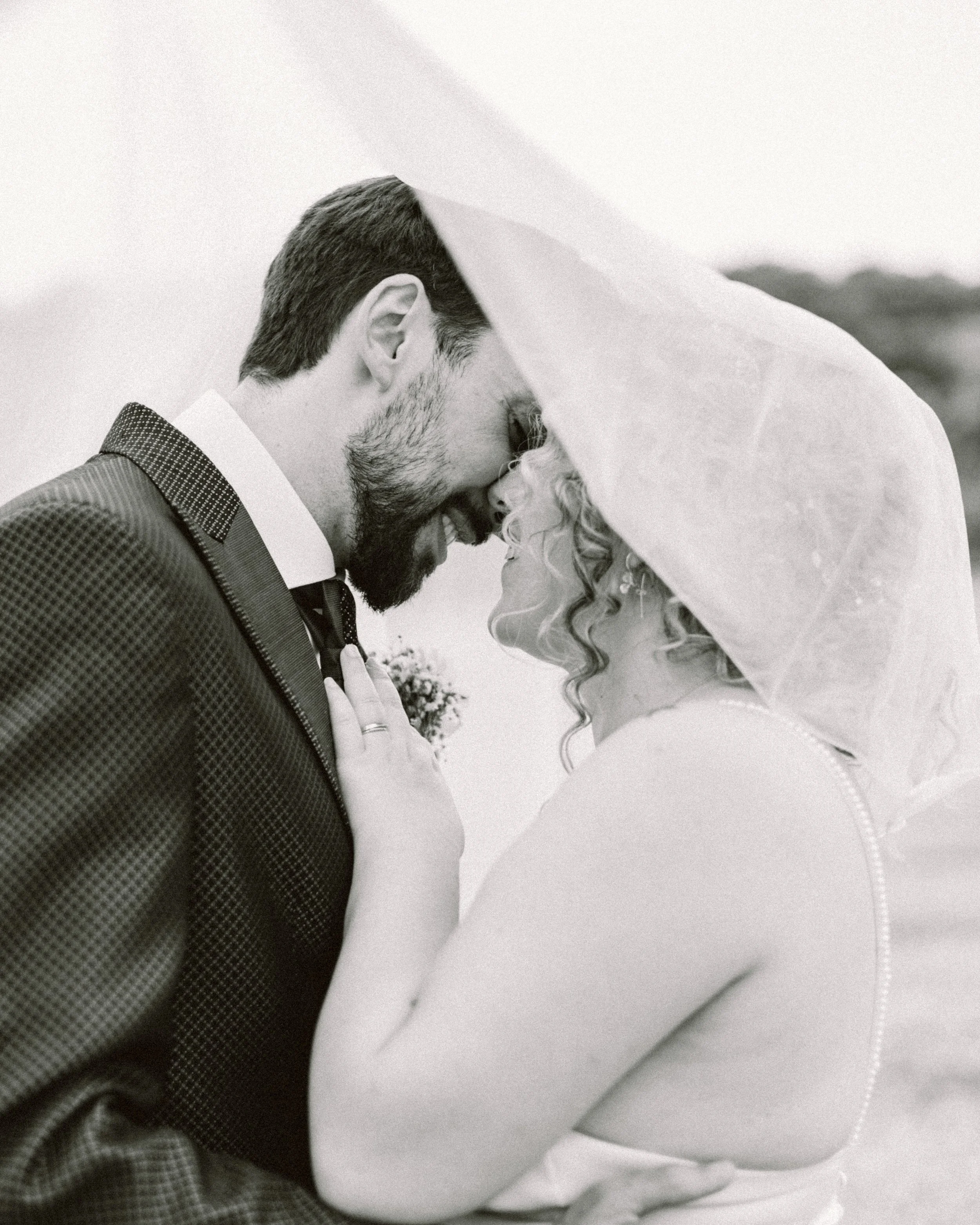 Pareja de novios en una boda bajo una sombrilla, con la frente juntas y sonriendo.