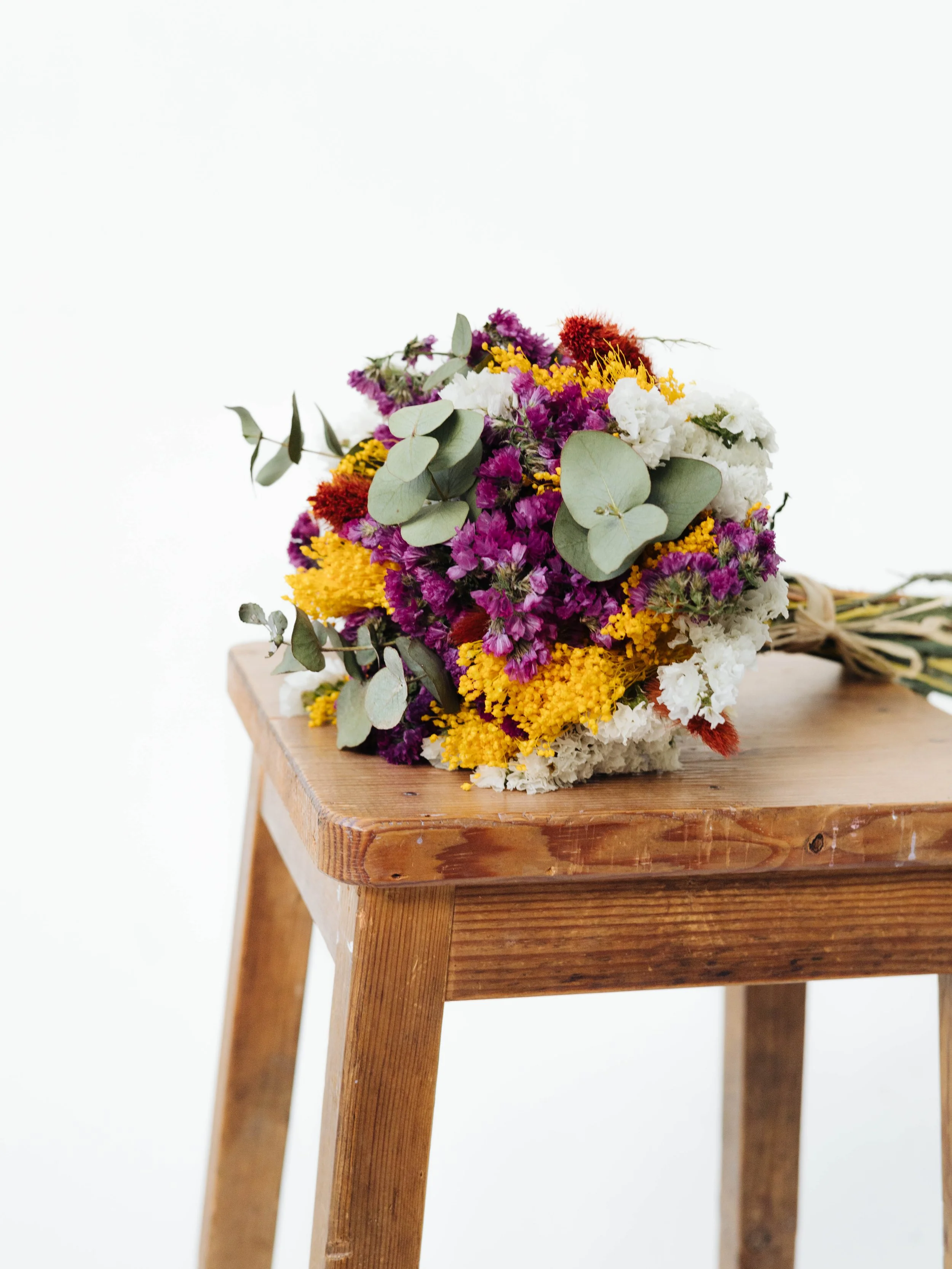 Ramo de flores coloridas con flores moradas, amarillas, blancas y rojas, con hojas verdes, descansando sobre una mesa de madera.