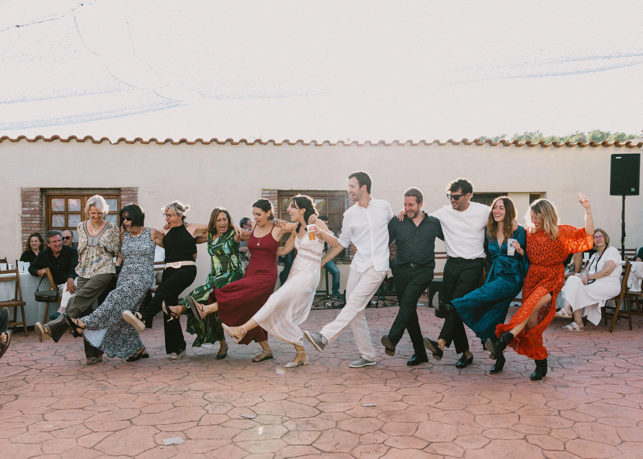 Un grupo de personas bailando en una celebración al aire libre, con risas y alegría visible en sus rostros.