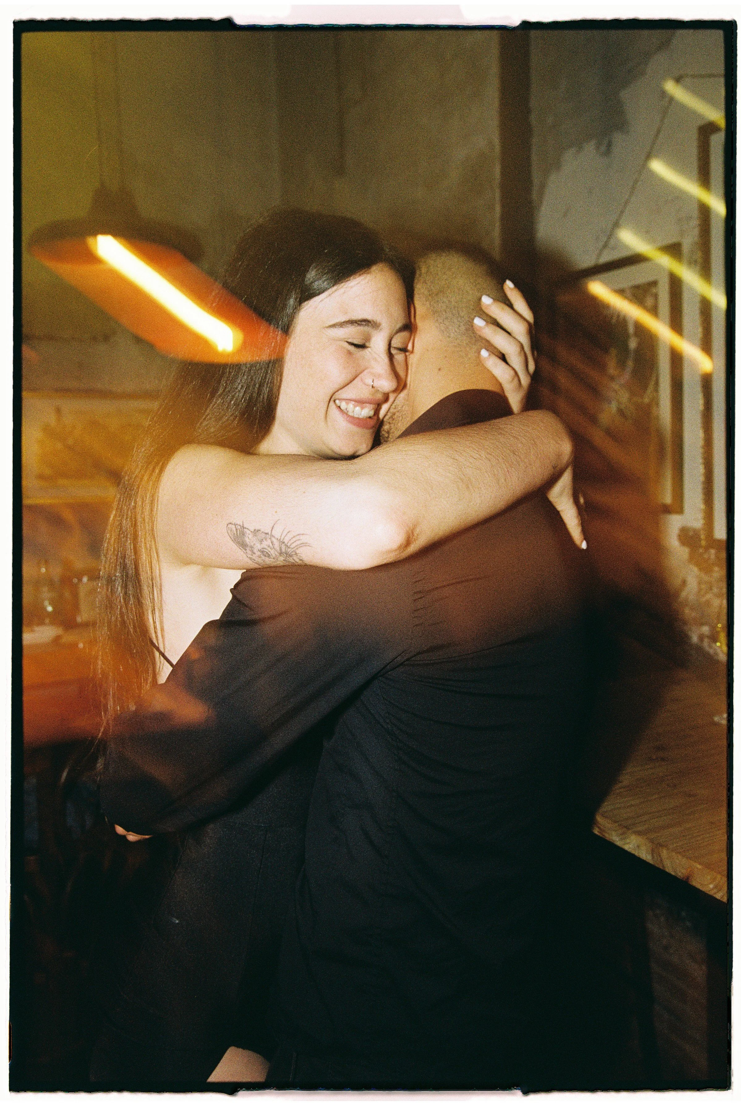 Dos personas abrazándose con alegría en un ambiente cálido y acogedor, con luz de neón y decoración moderna.