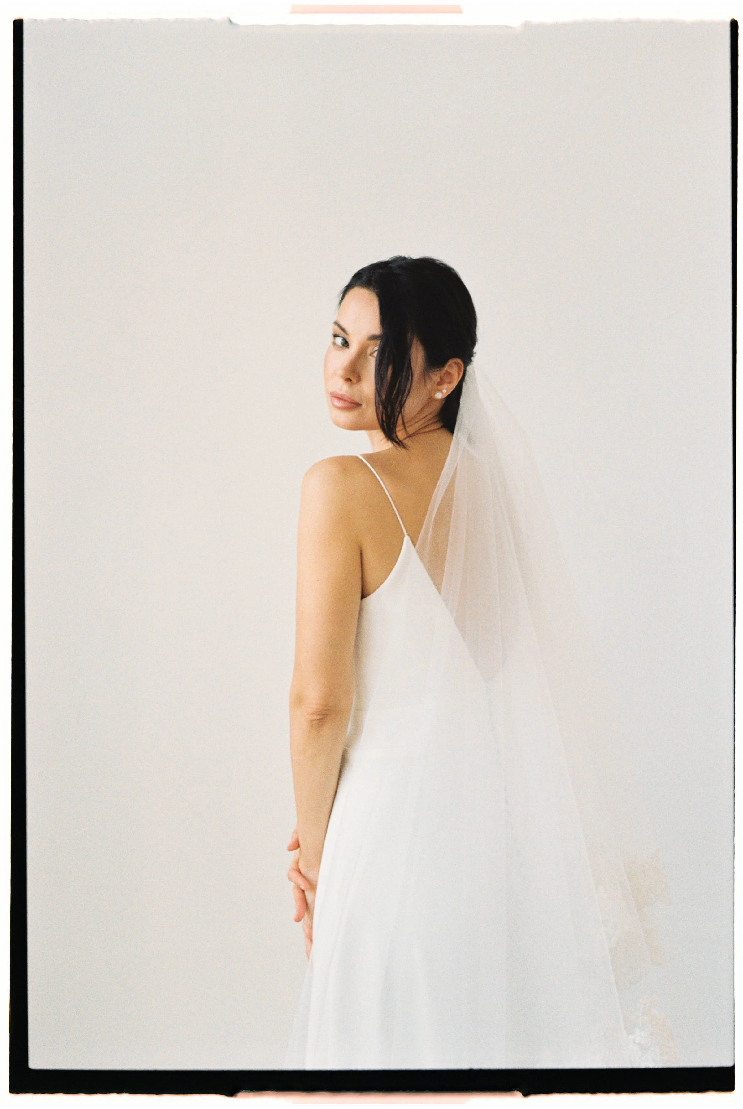 Mujer con vestido de novia y velo, posando en fondo blanco.