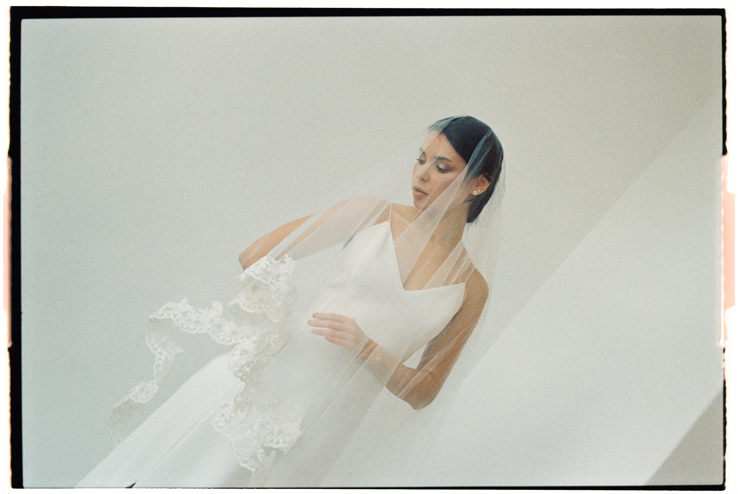 Mujer con vestido de novia y velo, mirando hacia abajo, en un fondo claro.
