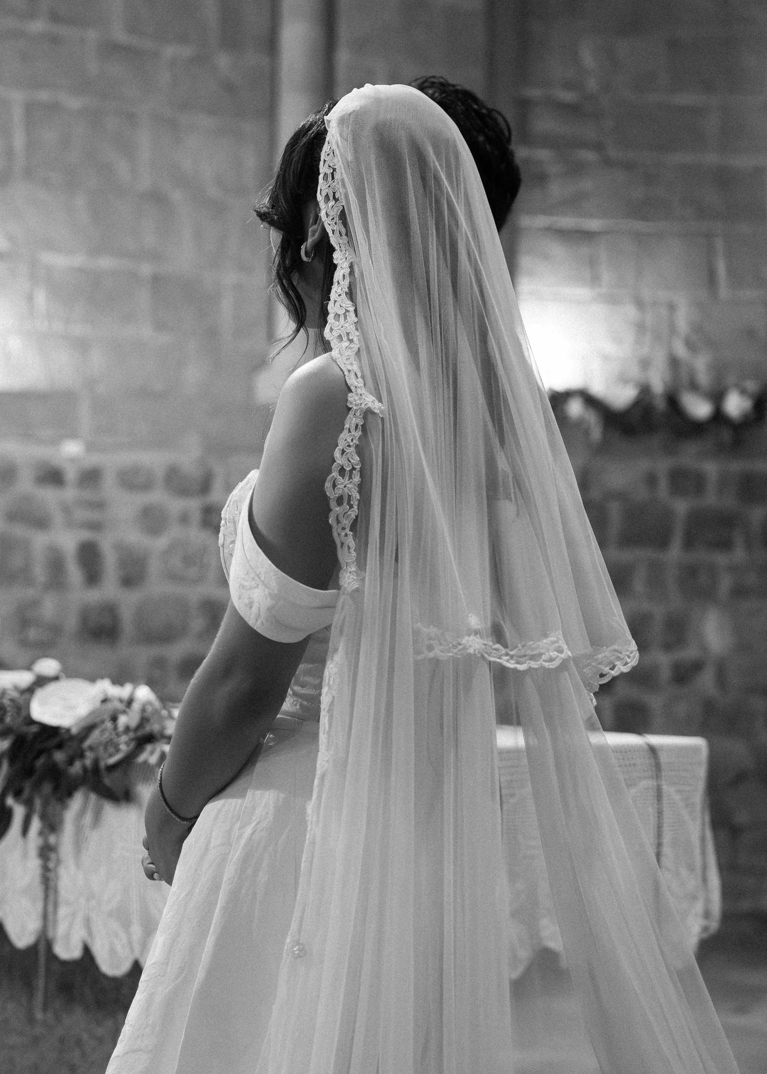 Mujer con vestido de novia y velo en un lugar con paredes de ladrillo y decoraciones florales.