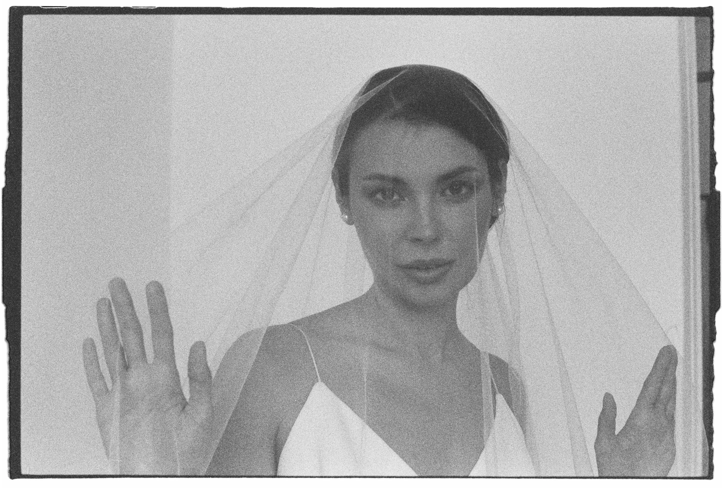 Mujer con vestido de novia y velo, posando con las manos sobre un cristal.