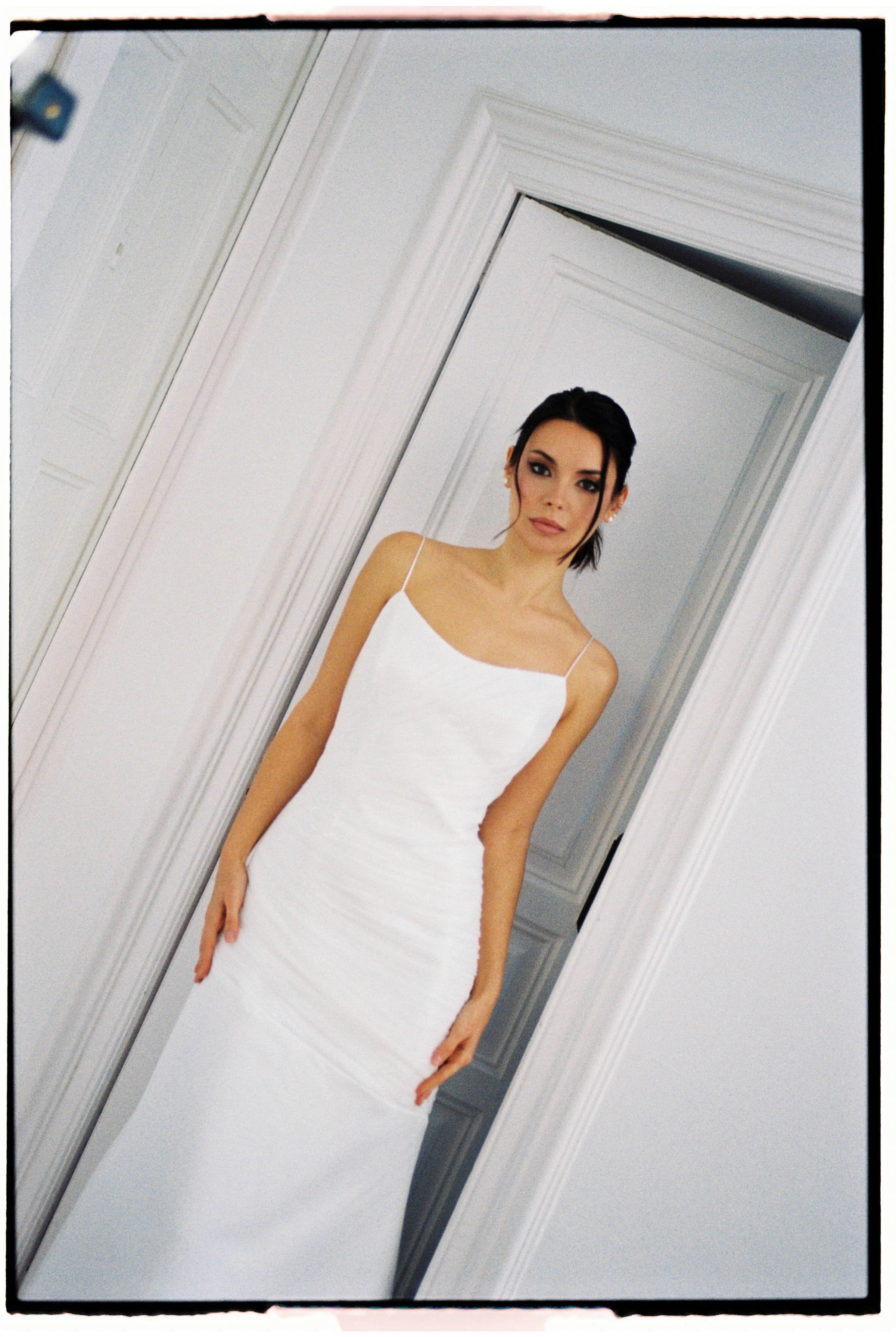 Mujer con vestido blanco de noche en el interior de una casa, parada frente a una puerta