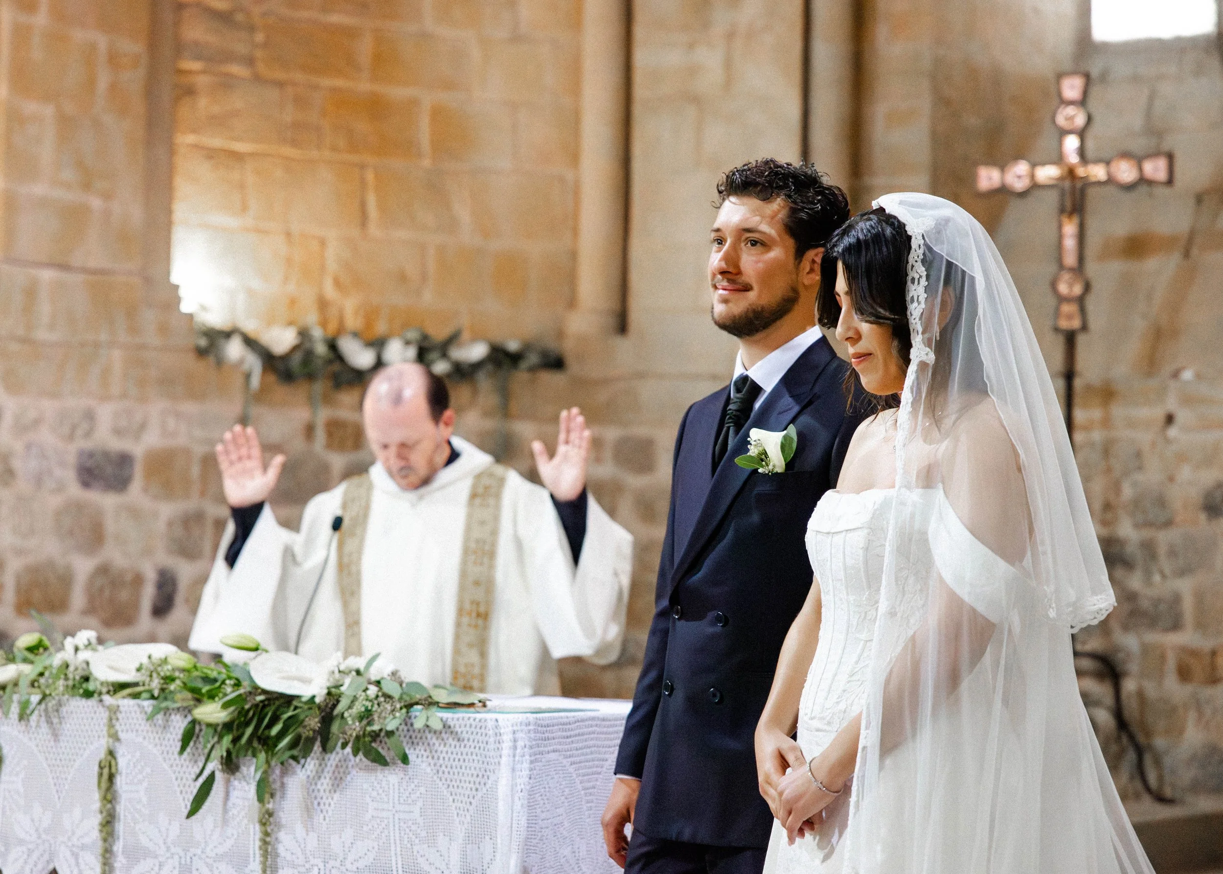 Una pareja casándose en una iglesia con una ceremonia religiosa, de pie frente al altar, con una vela y una cruz en el fondo.