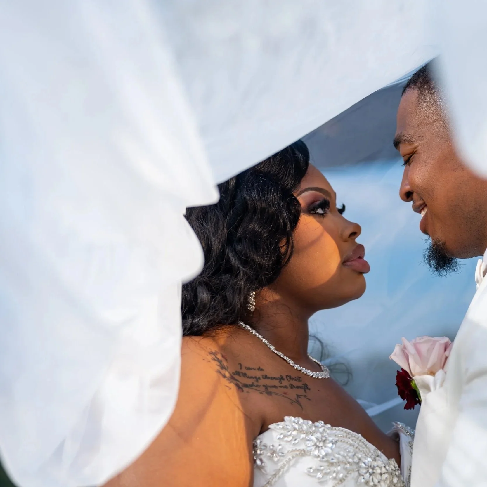 A bride and groom facing each other under a white veil during their wedding ceremony.
