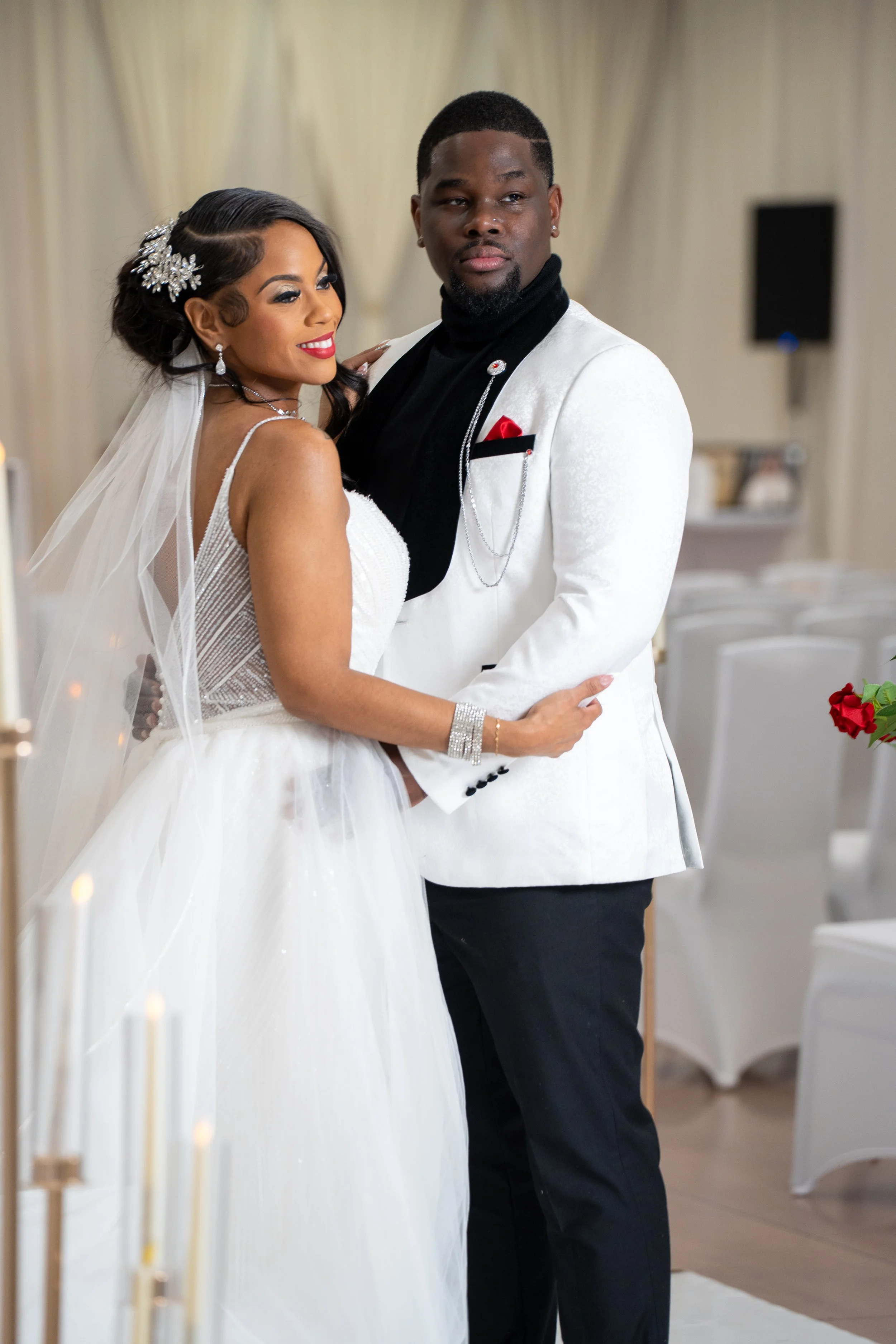 A bride and groom dancing at their wedding reception in an indoor venue with white chairs and beige curtains.