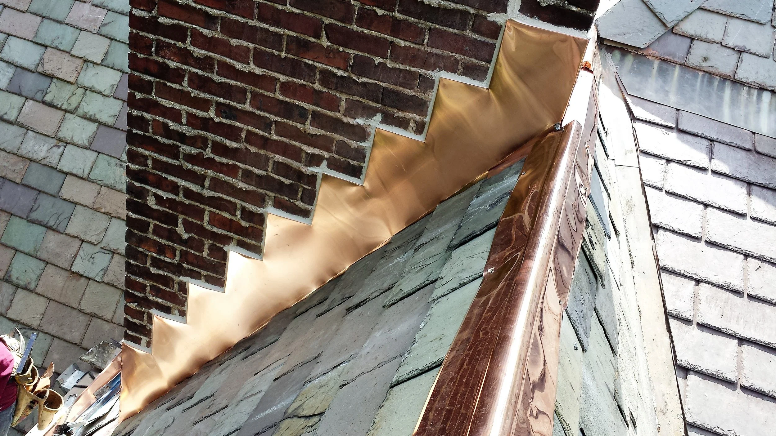 Stair-stepped copper chimney flashing tied into a copper ridge detail on a slate roof.