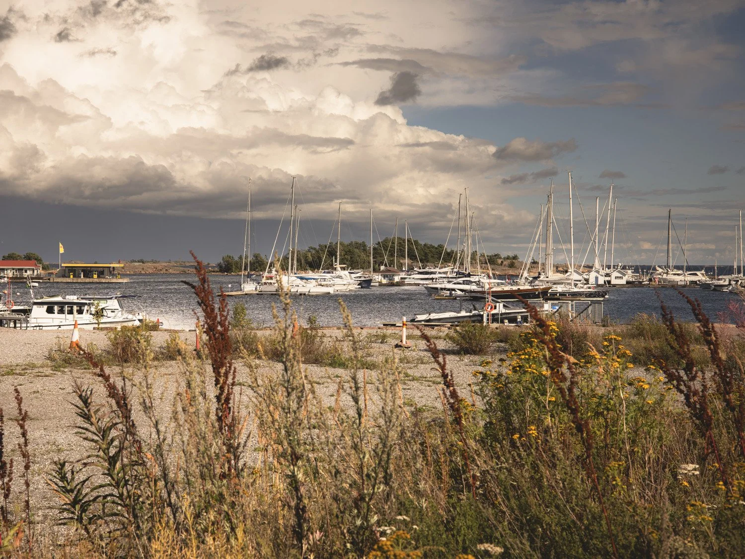 Sailboats and yacht masts in a harbour beneath expansive cloudy skies, creating a sense of journey and horizon.
