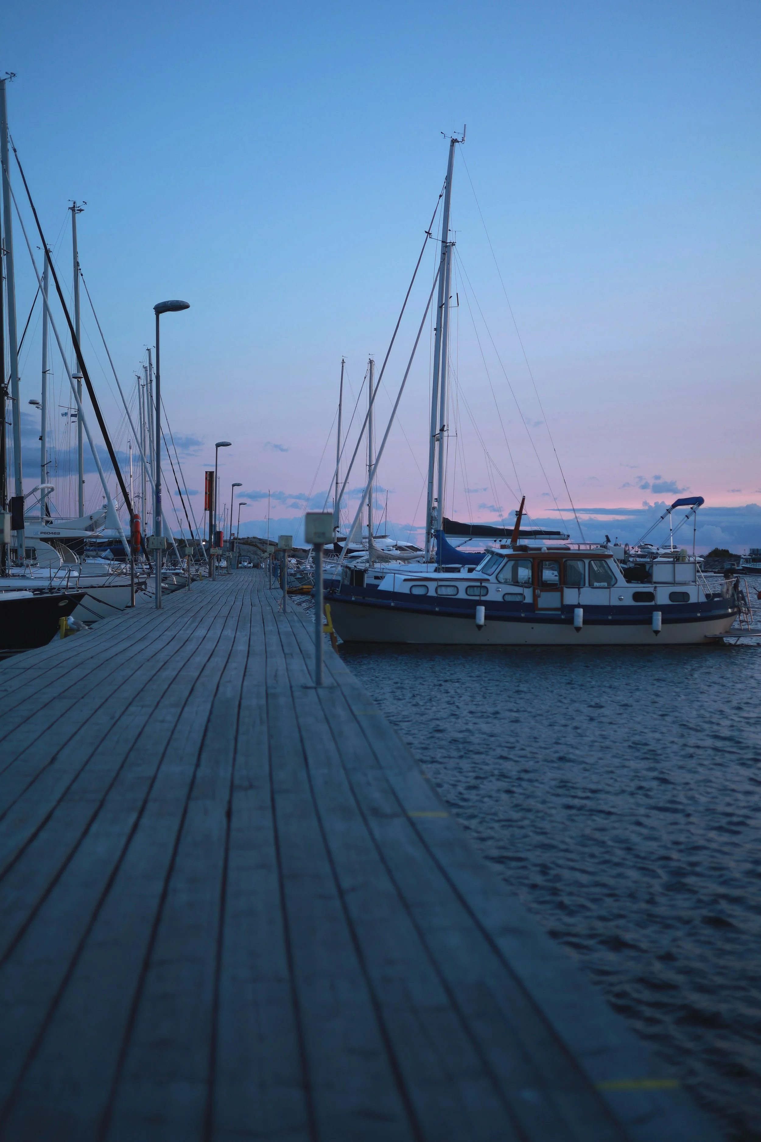 Wooden harbour pier stretching forward between boats during blue hour.