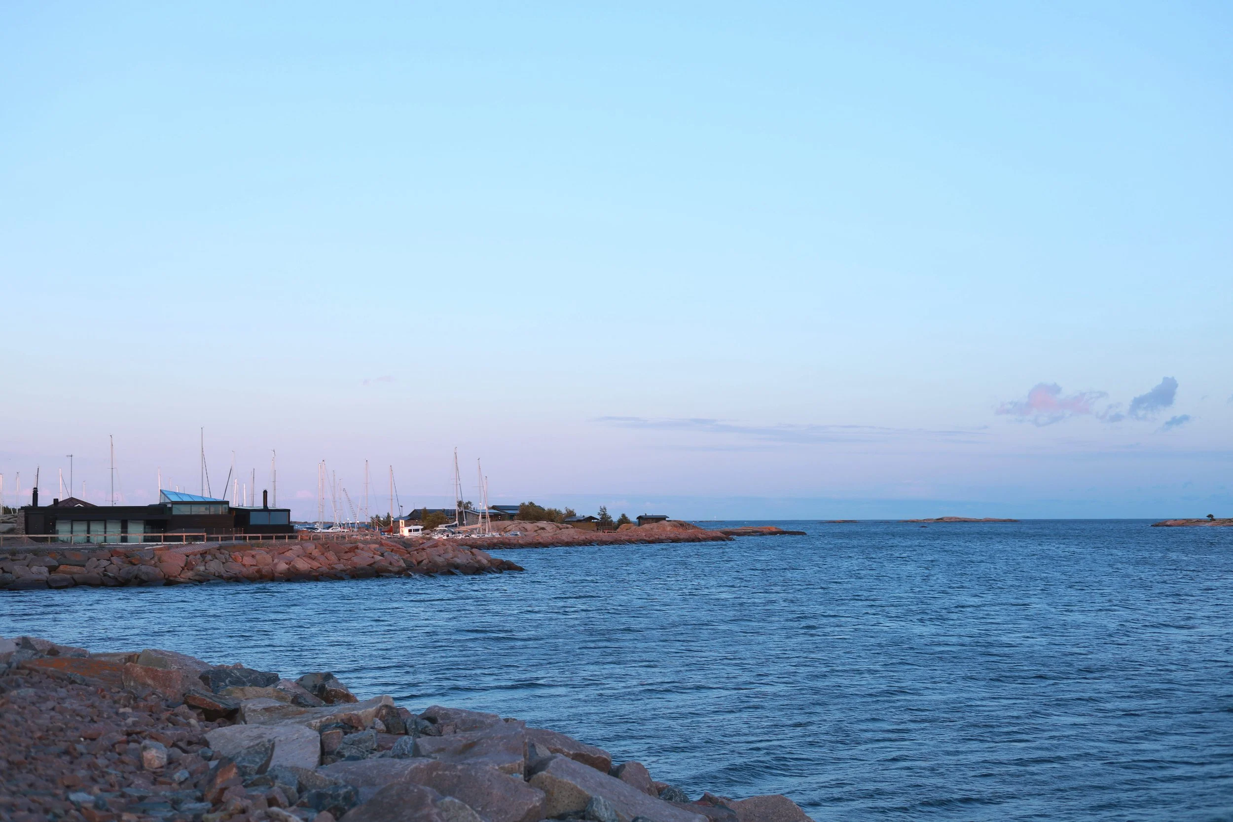Calm blue-hour sea beneath a pale blue and pink sky with the harbour in the distance.