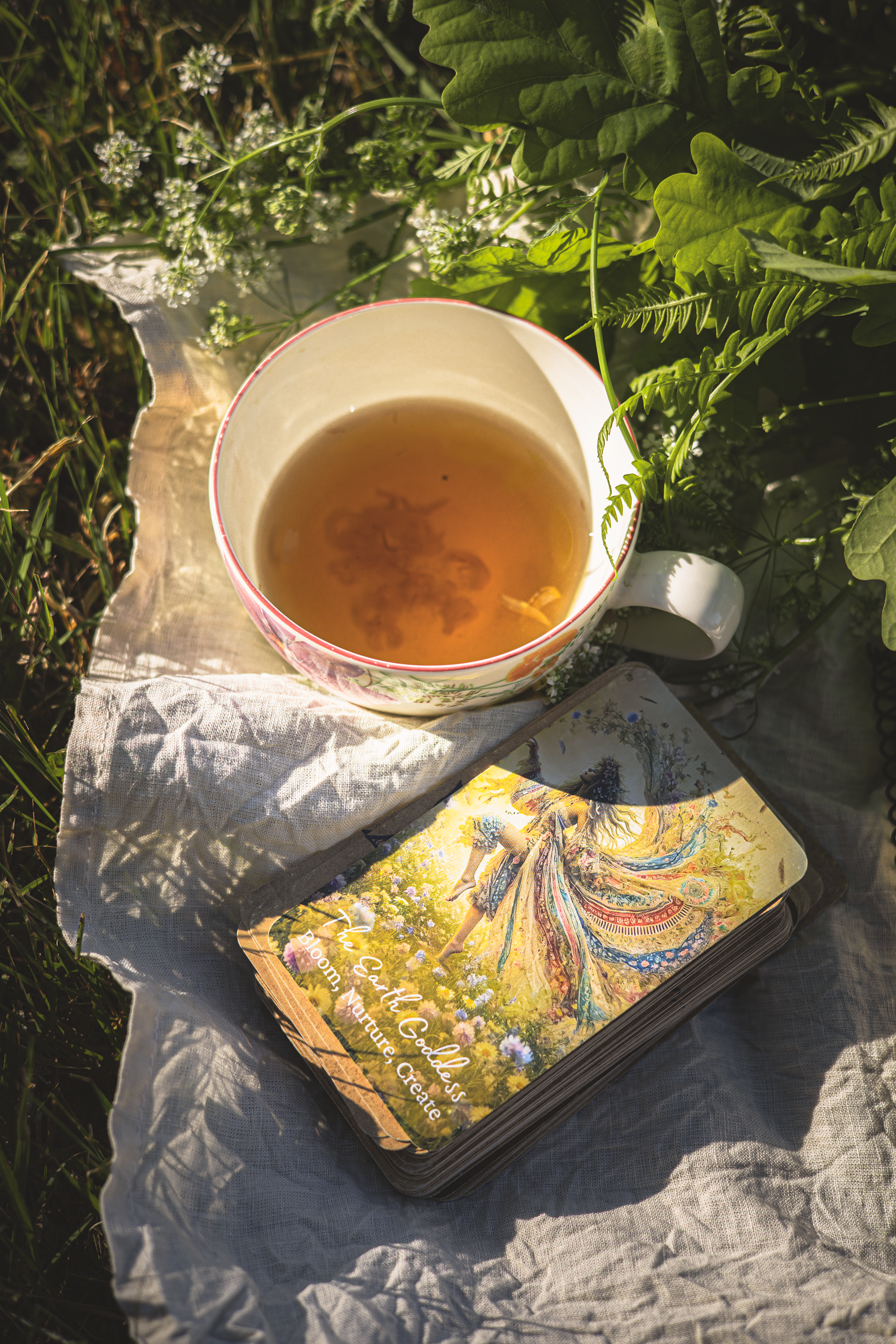 The Earth Goddess card beside a cup of tea in nature