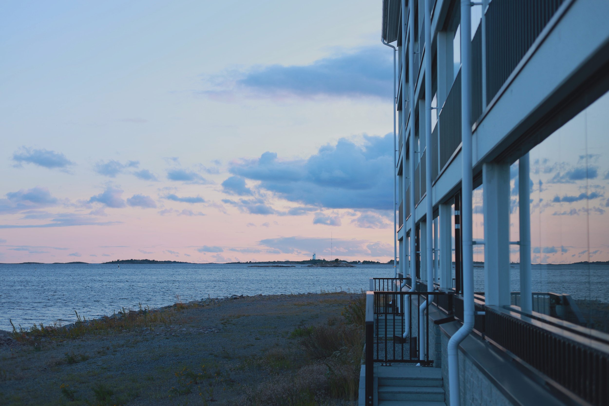 Sea beside a waterfront building as the evening light turns cool blue and pink.