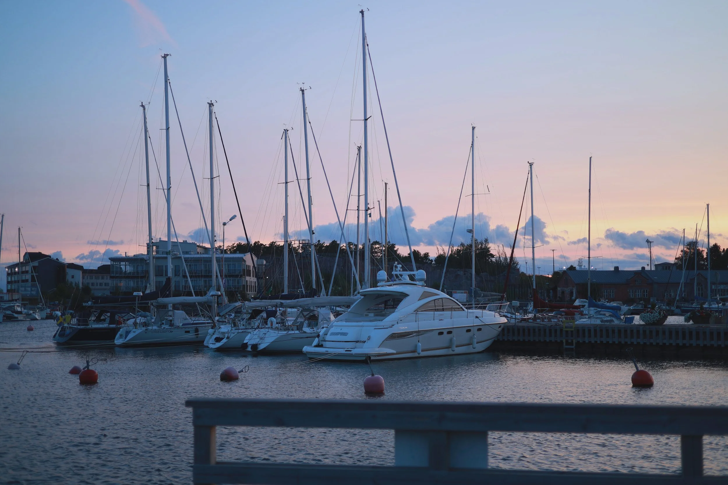 Boats and sailboat masts in the harbour during blue hour under a fading pastel sky.
