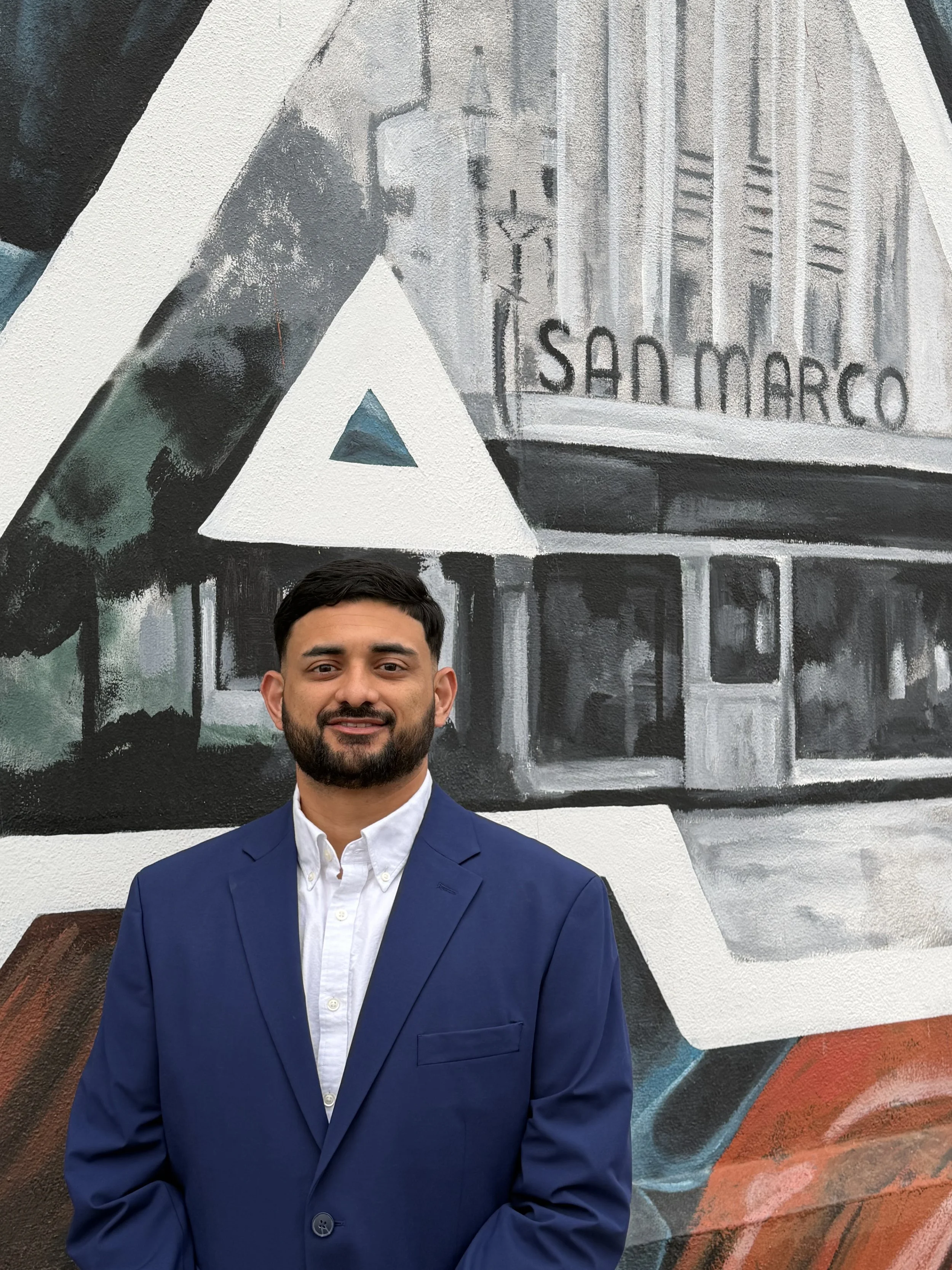 A man dressed in a blue suit and white shirt standing in front of a colorful mural on a wall. Jacksonville, Fl. San Marco Jacksonville