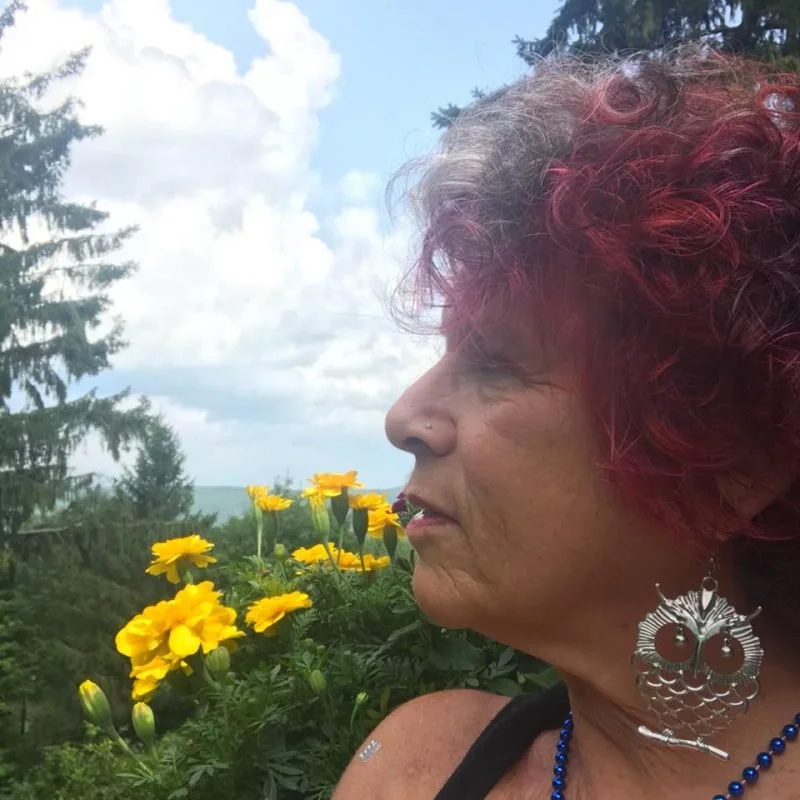 A smiling woman with long dark hair, wearing a dark-colored top, standing indoors.