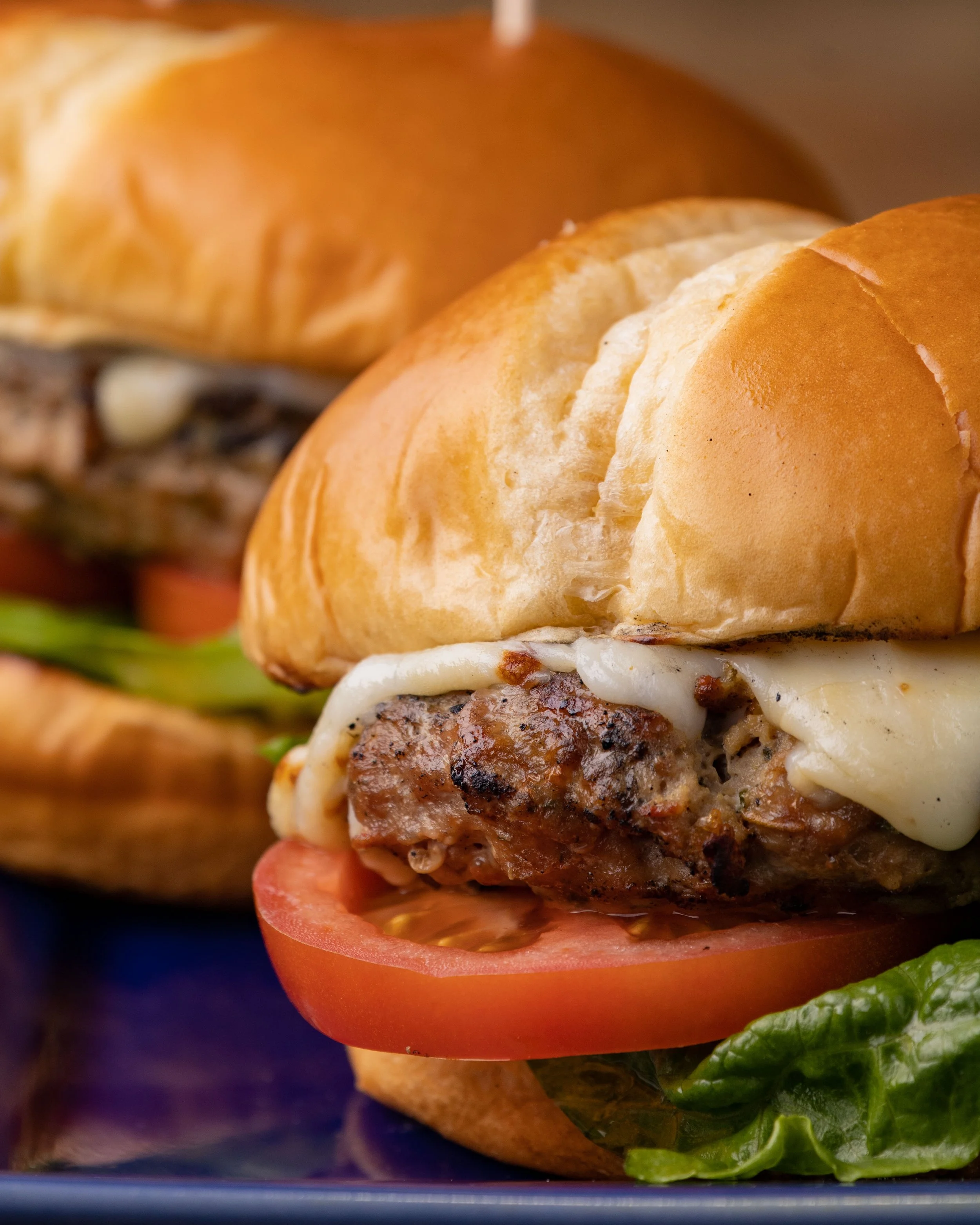 Close-up of a cheeseburger with tomato, lettuce, grilled beef patty, and melted cheese in a bun.