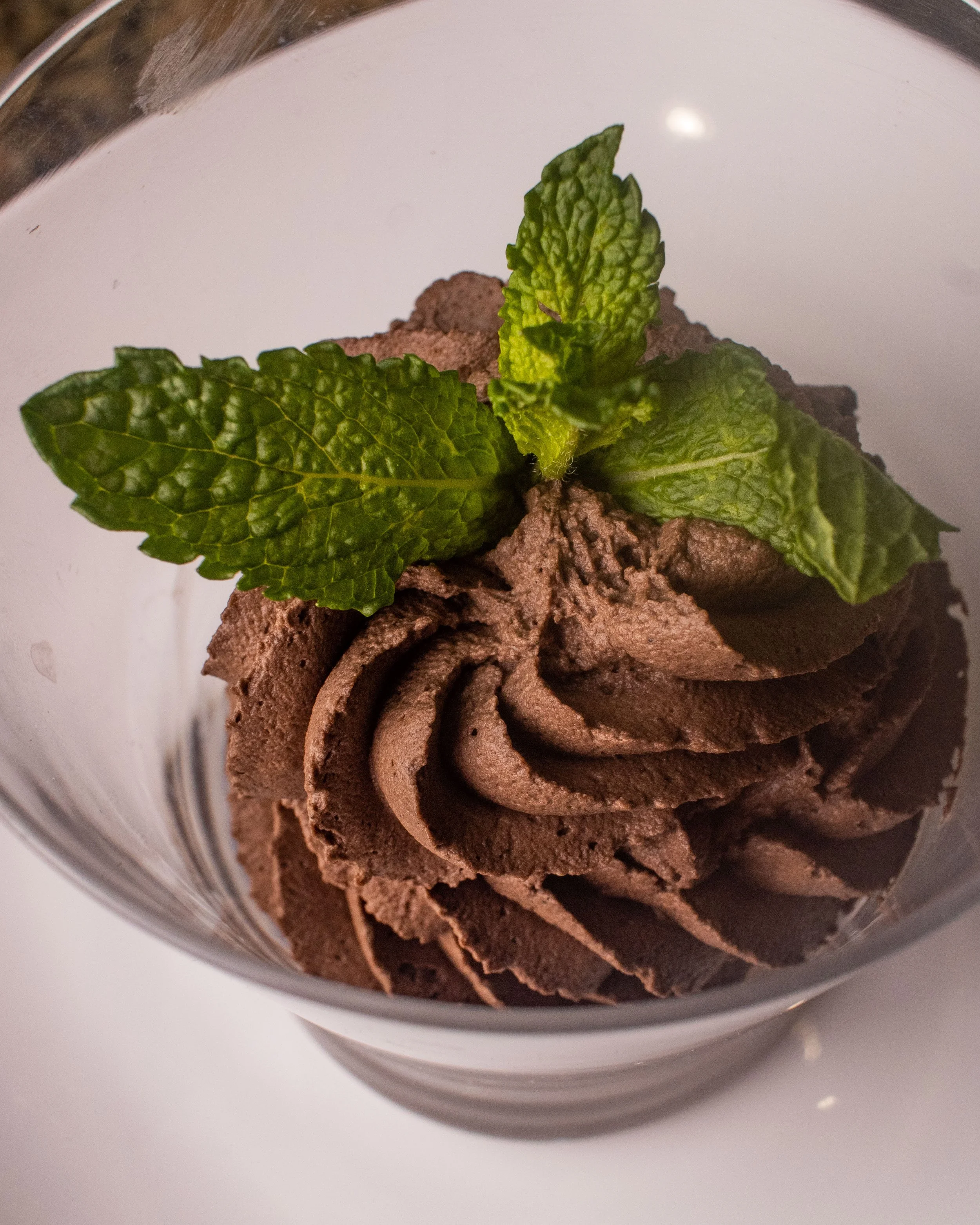 Chocolate mousse topped with fresh mint leaves in a glass bowl.
