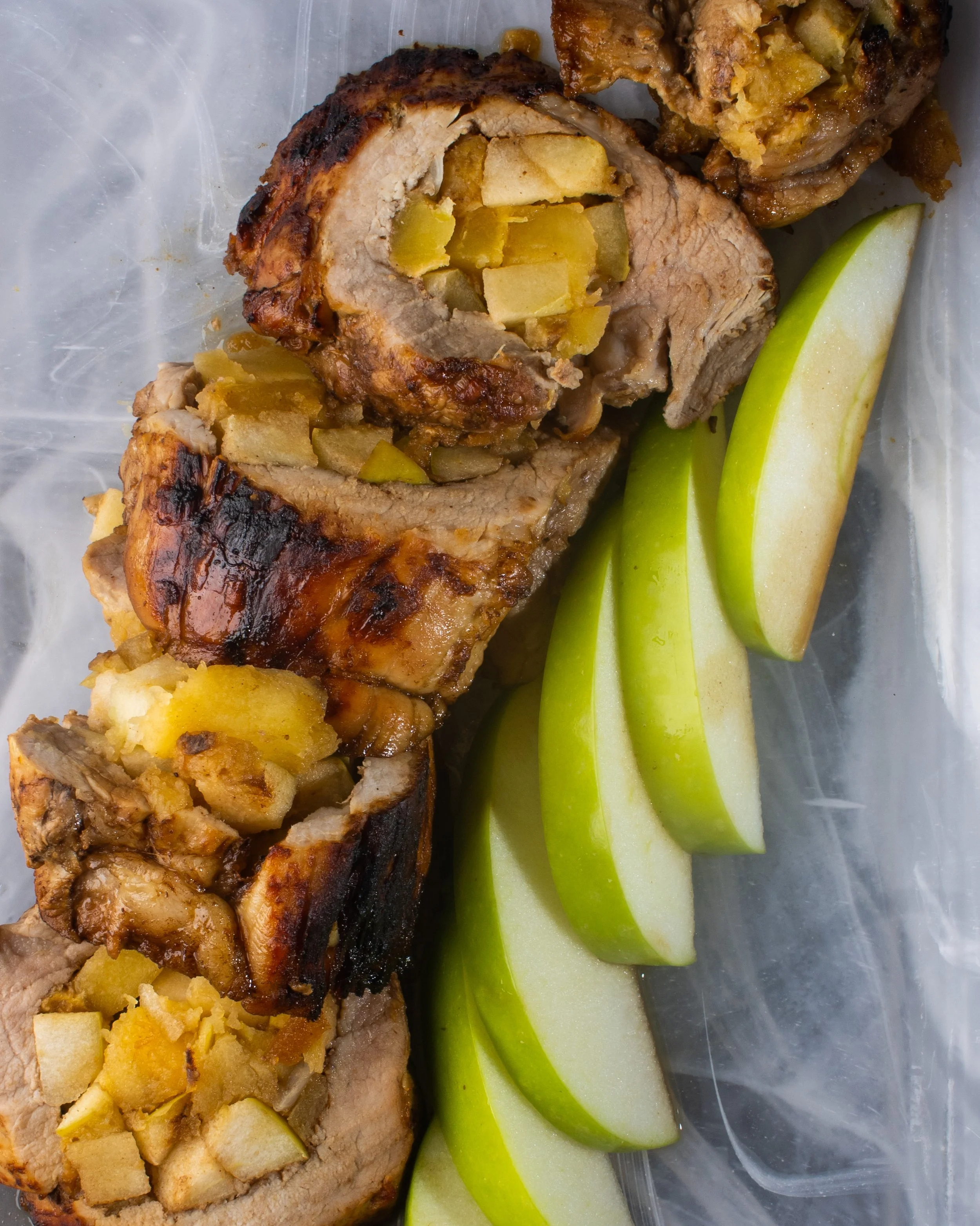 Stuffed pork tenderloin slices with diced apples, green apple wedges on a tray.