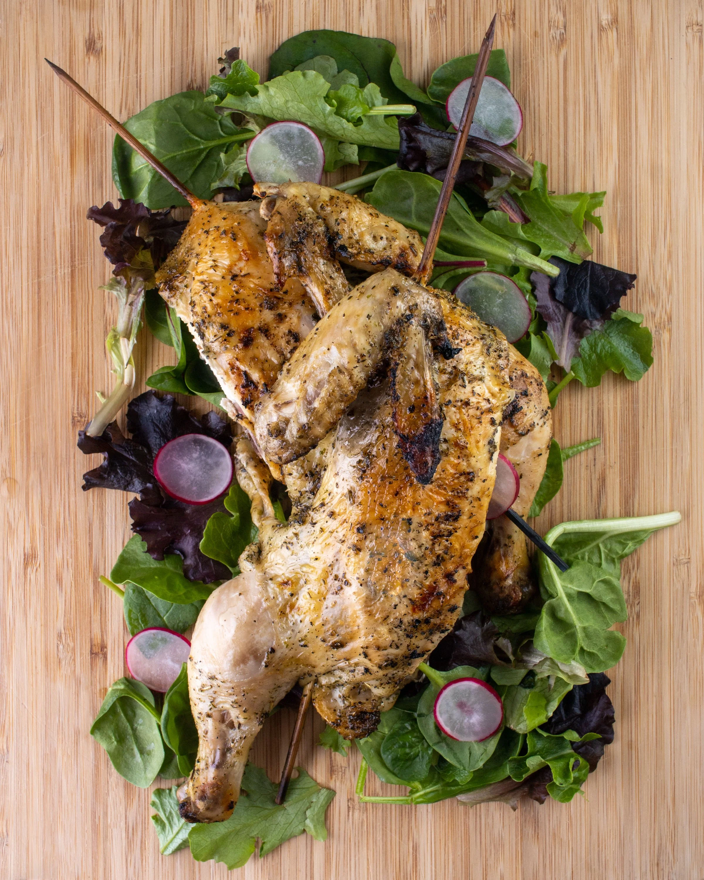Whole roasted chicken on a cutting board garnished with fresh greens and sliced radishes.