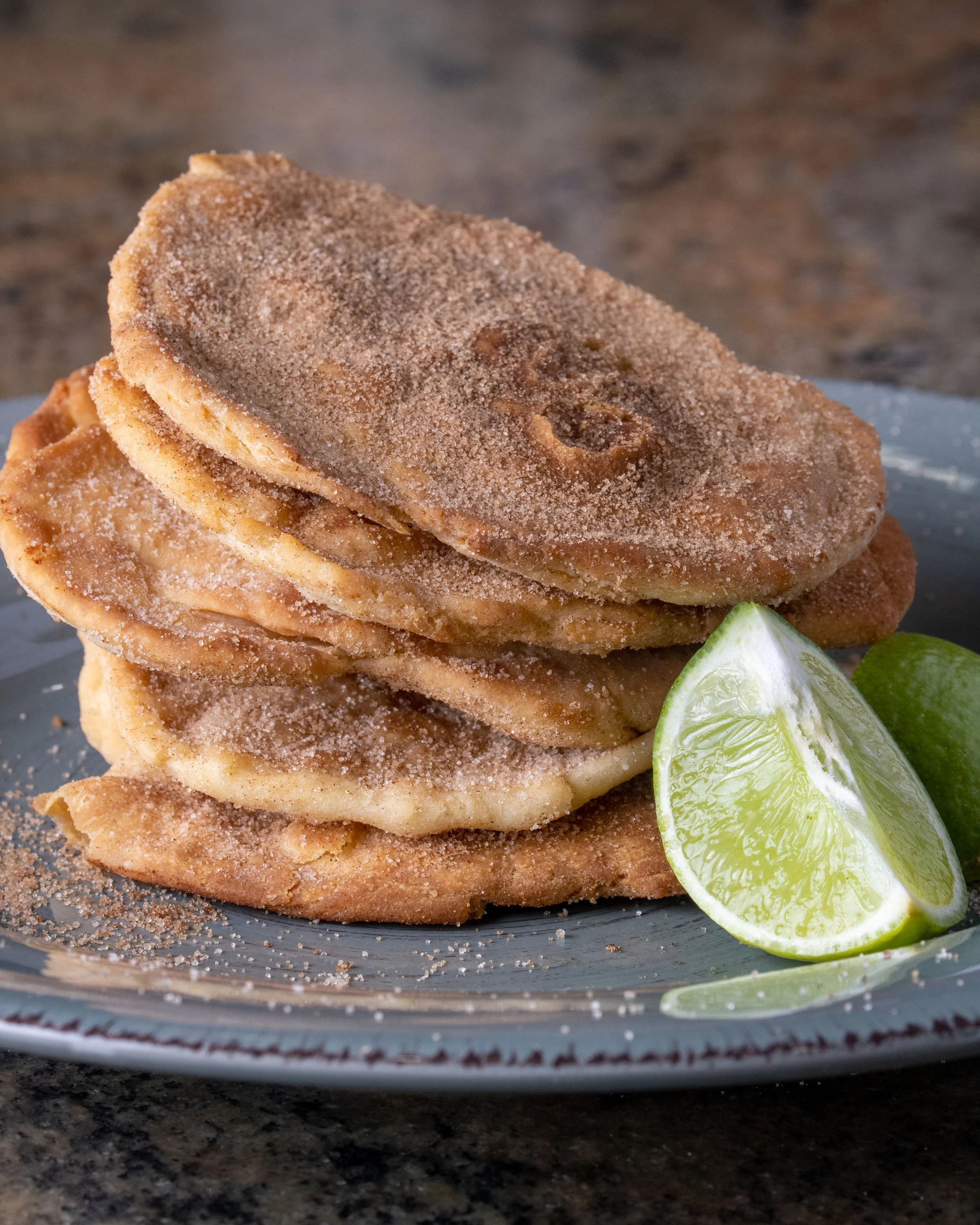 Stack of fried jaggery-sweetened banana fritters with two lime wedges on a plate.