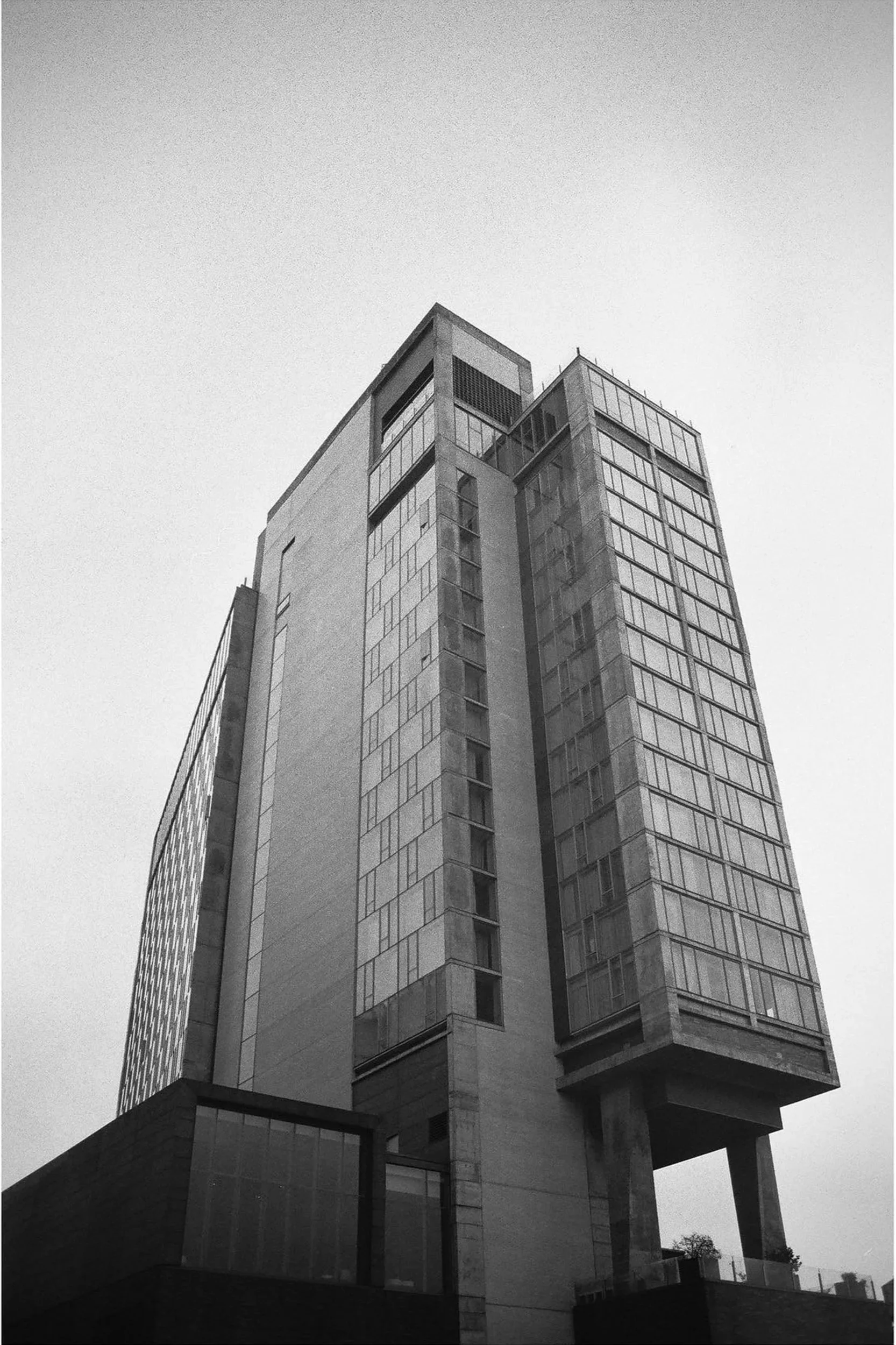 Black and white photo of a modern high-rise building with large glass windows, viewed from a low angle.