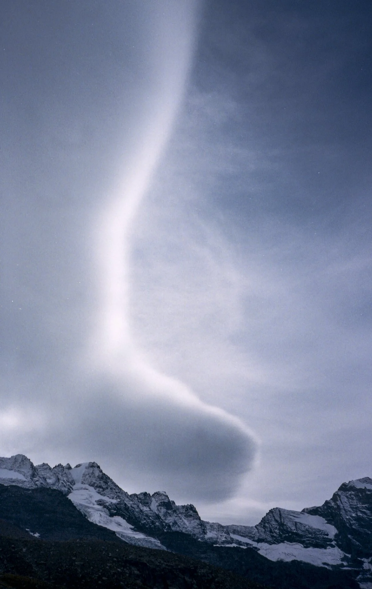 Night sky with a bright, elongated lightning bolt striking above snow-covered mountain peaks.