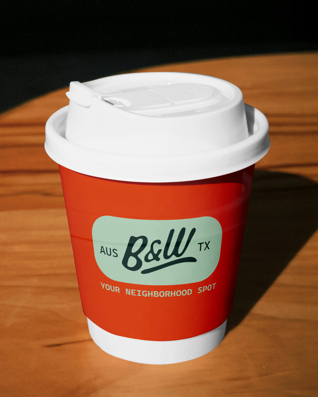 A disposable coffee cup with a red sleeve and white lid, sitting on a wooden surface.