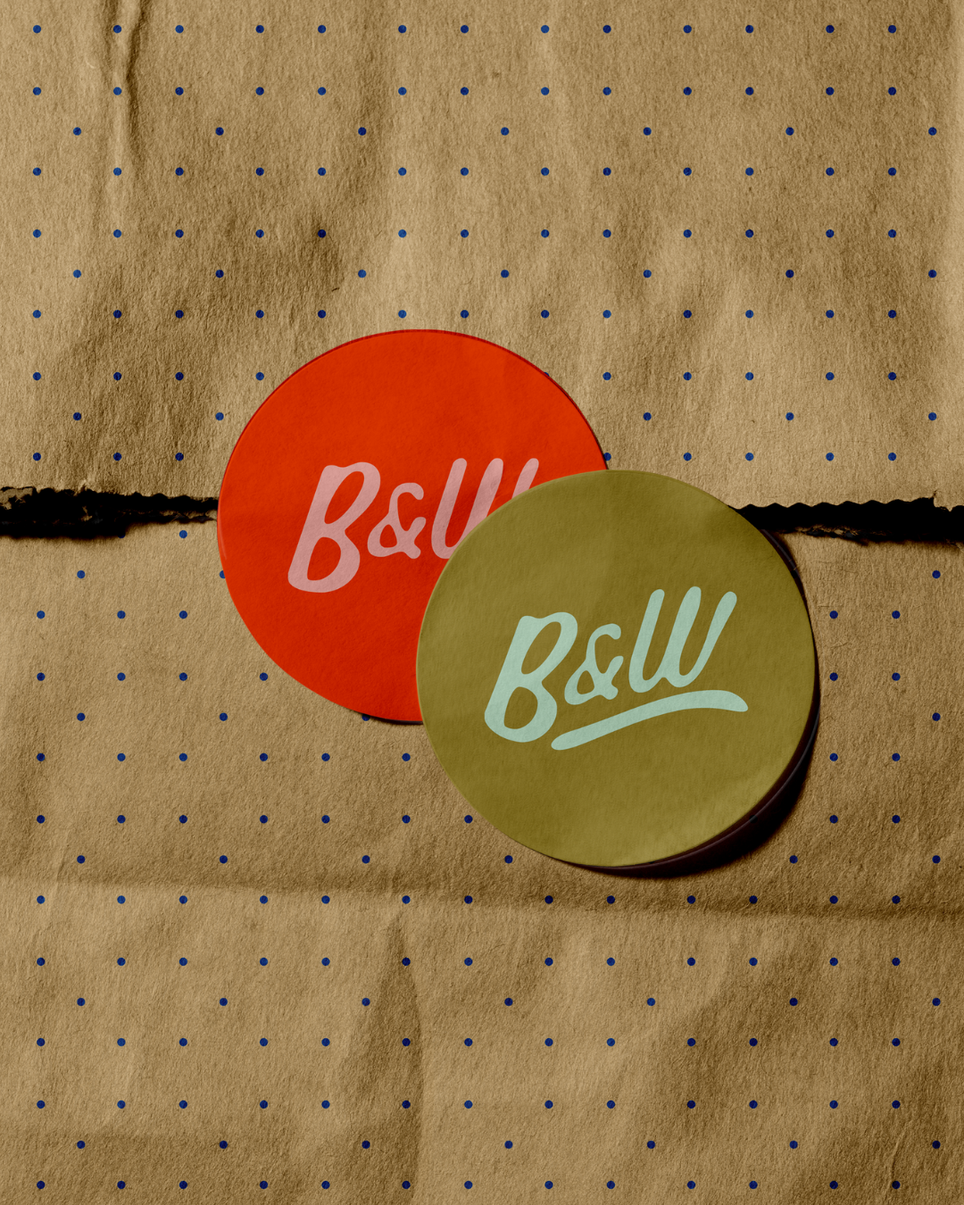 Two circular objects, one red and one yellow, with the B&W logo in pink and cyan respectively, placed on brown dotted paper.