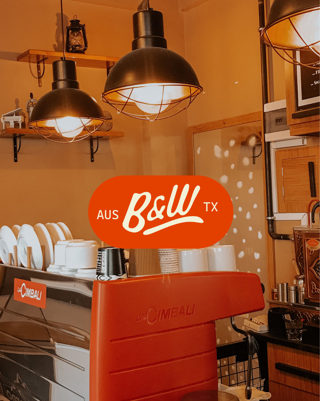 Interior of a coffee shop with modern lighting, a red La Cimbali espresso machine, white cups, and warm lighting.